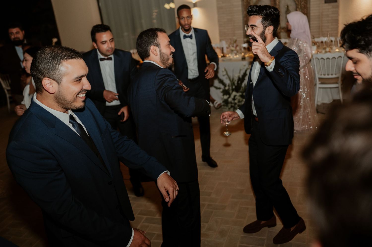 Elegantly dressed groomsmen socializing and laughing together at indoor wedding reception.