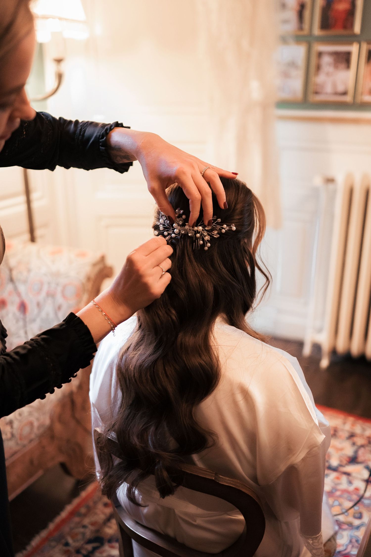 Hairstylist placing a floral hair accessory in the bride\u2019s dark wavy hair before the wedding.
