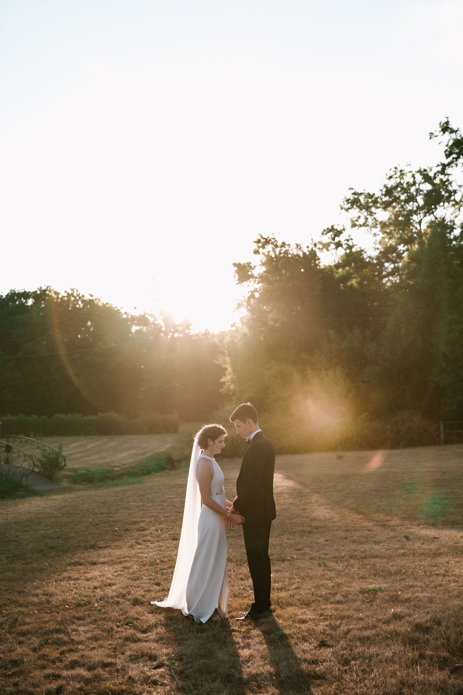 Bride and groom hold hands in golden sunset light in an open countryside field.