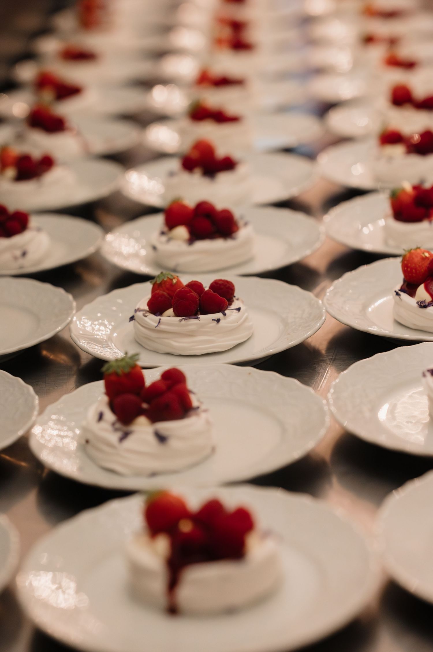 Rows of white plates with pavlova desserts topped with fresh strawberries and raspberries at wedding reception.