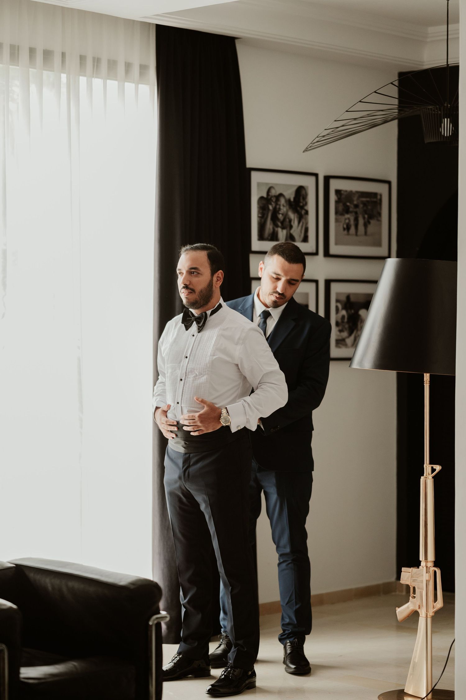 Groomsman helping groom adjust his white dress shirt before wedding ceremony.