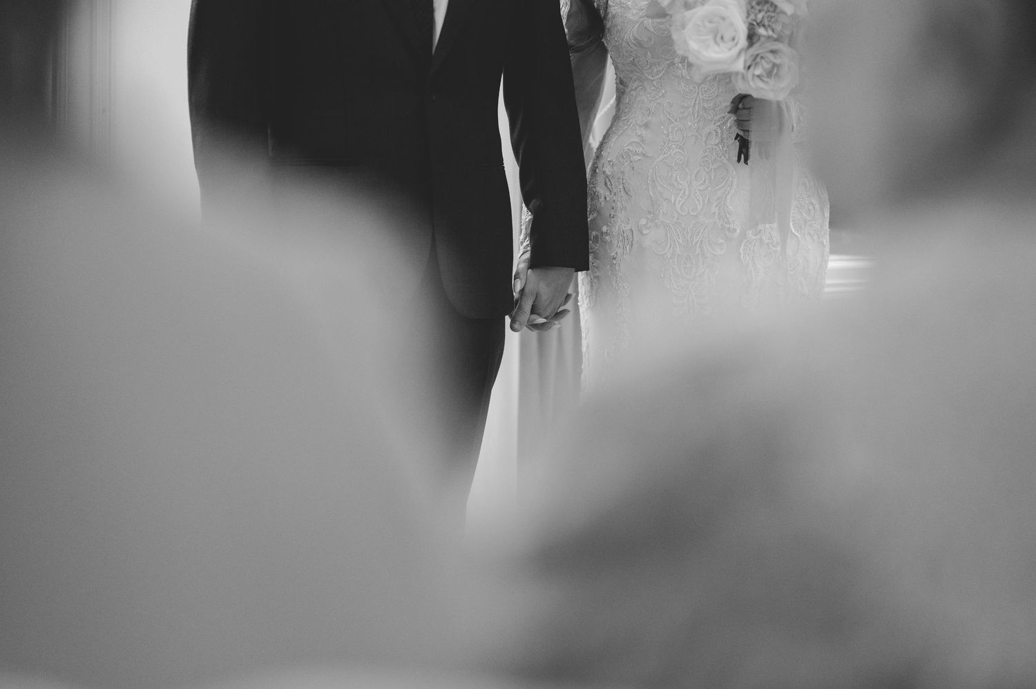 Bride and groom hold hands at the altar in an artistic black and white wedding photo.