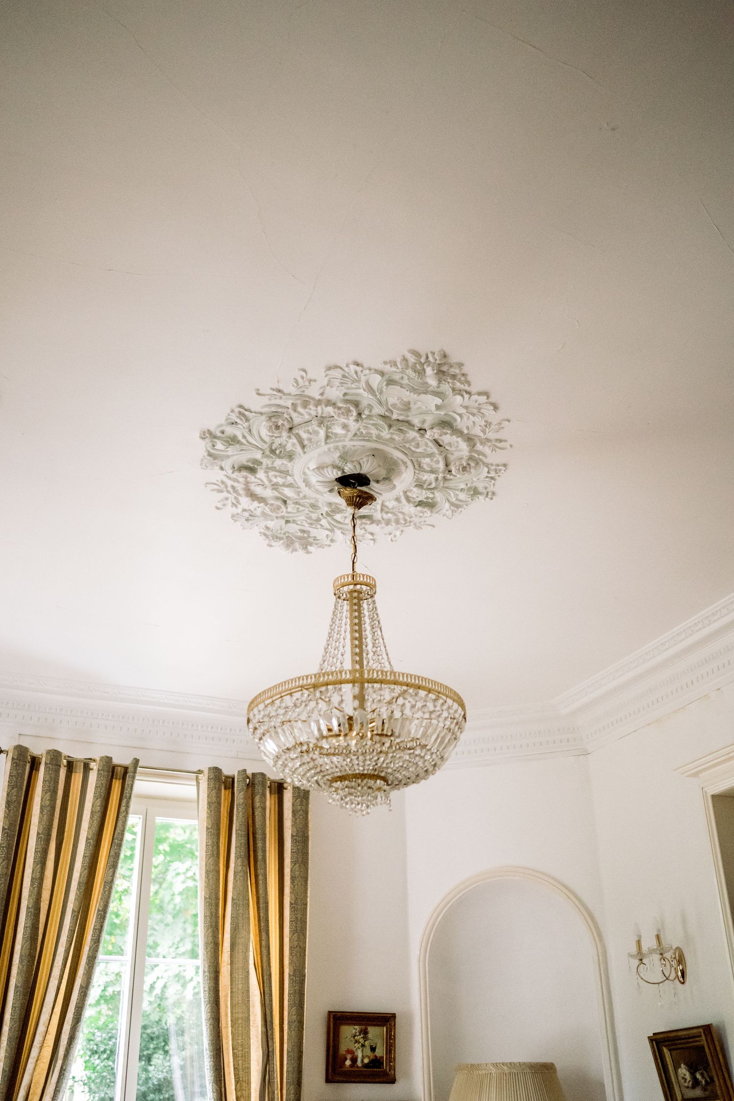 Elegant white ceiling with intricate plaster medallion and gold empire crystal chandelier in a classic French room.
