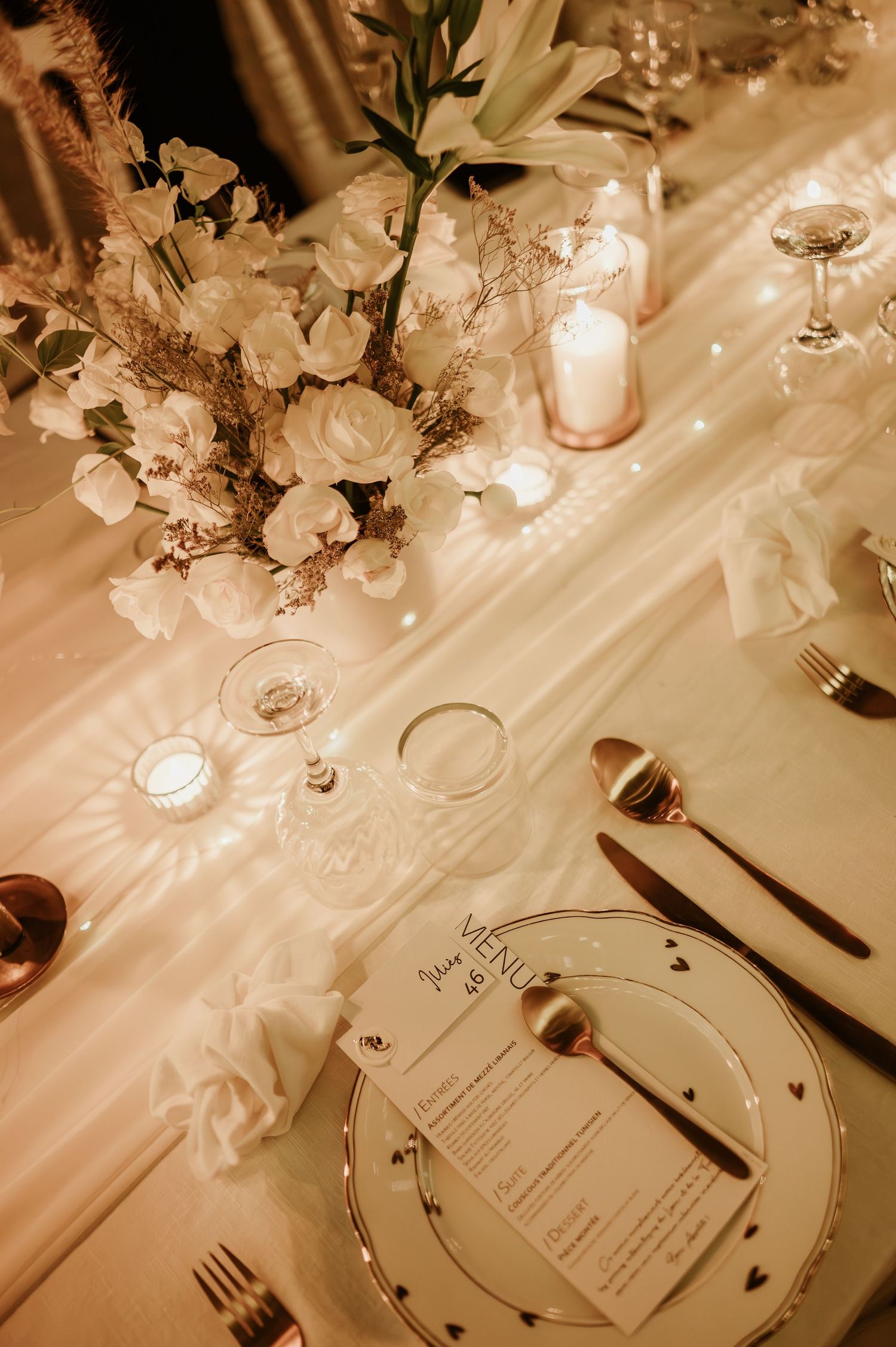 Wedding reception table with white floral arrangements, candles, glassware, and a personalized menu card.