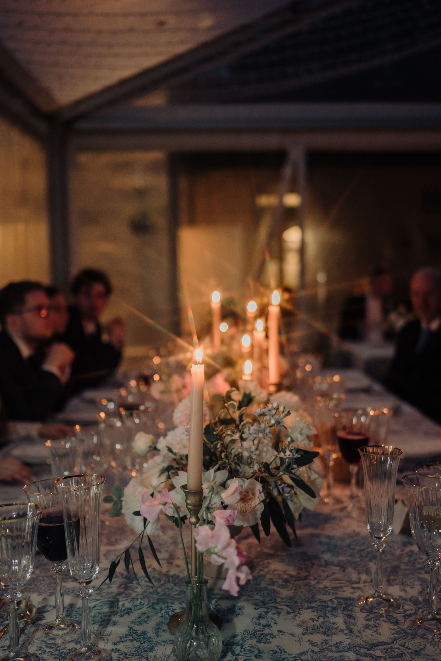 Romantic candlelit wedding reception table with white floral centerpieces and twinkling lights in an evening setting.