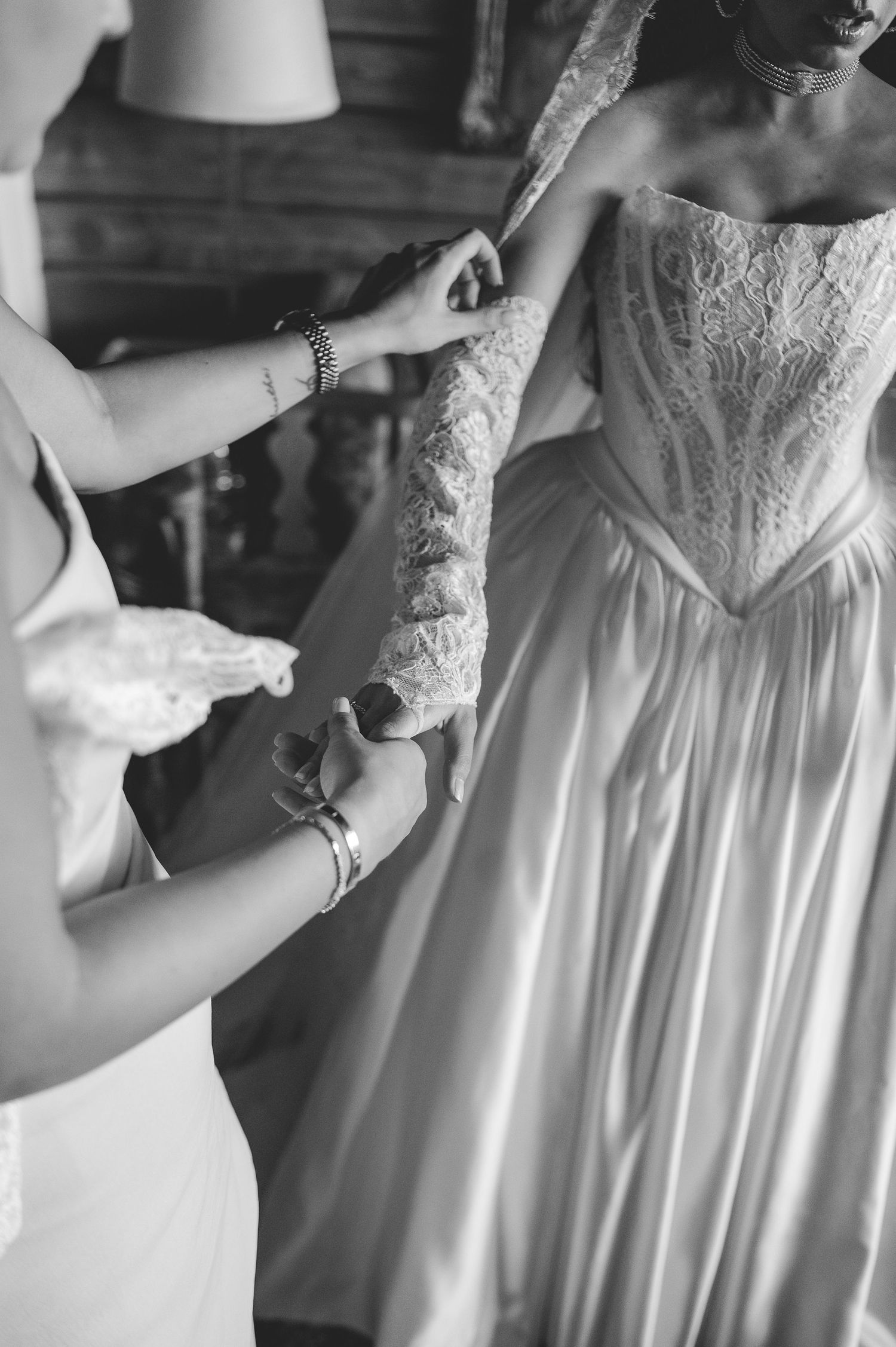 Black and white close-up of bridesmaid fastening lace sleeve detail on brides wedding gown.