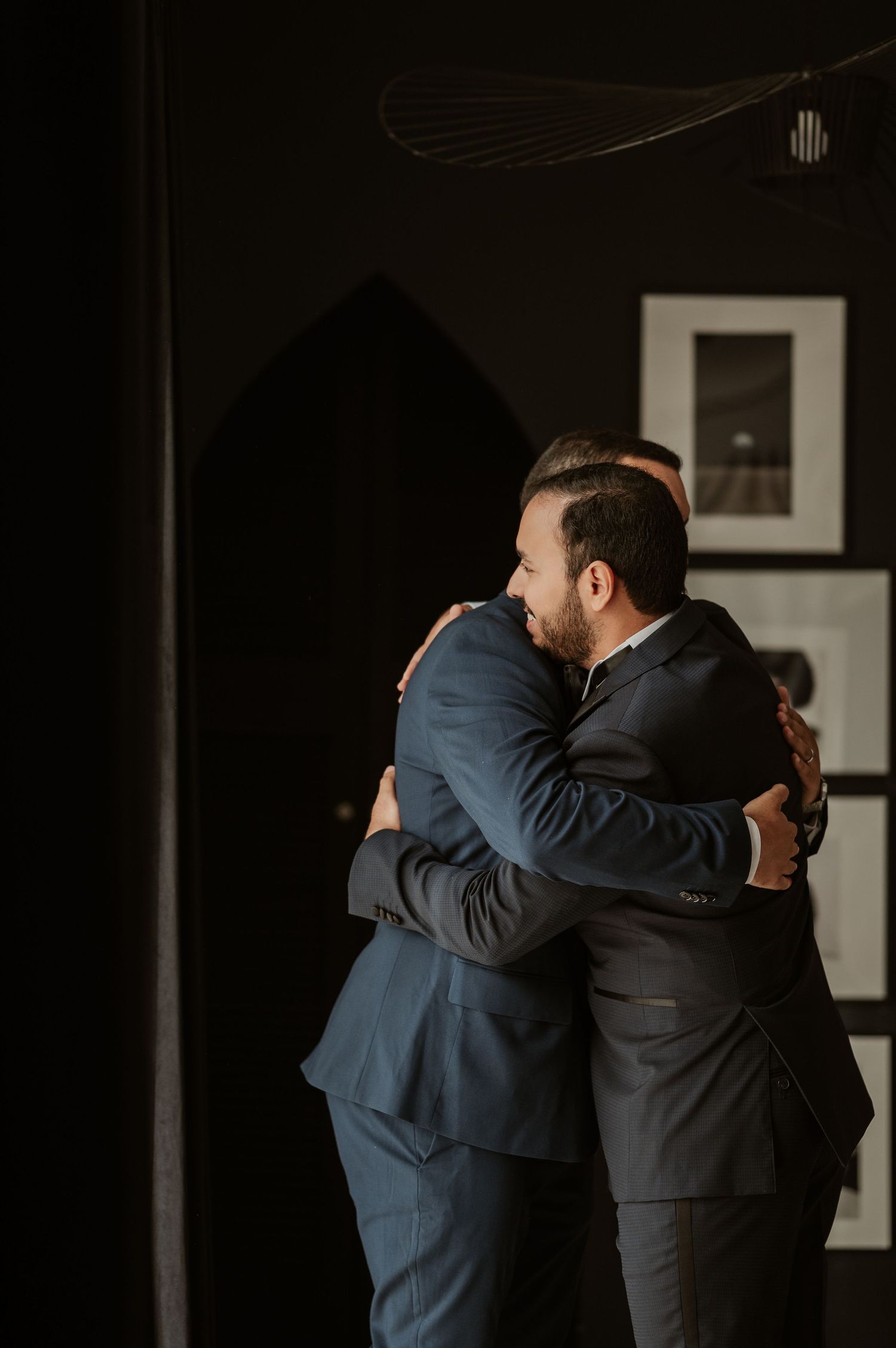 Two men in suits sharing warm embrace during wedding day preparations.