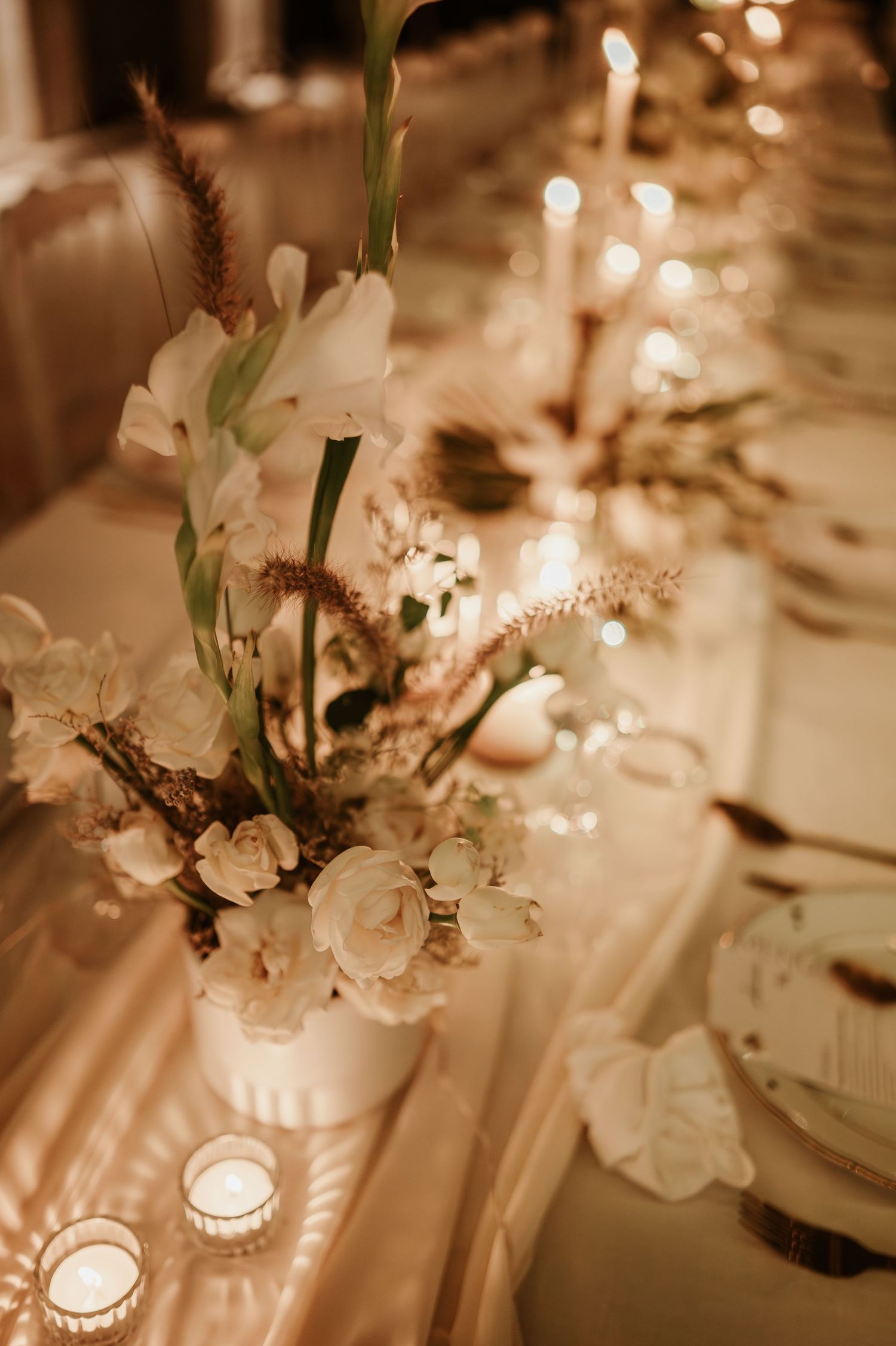 Elegant wedding table centerpiece with white flowers, candles, and warm golden lighting.