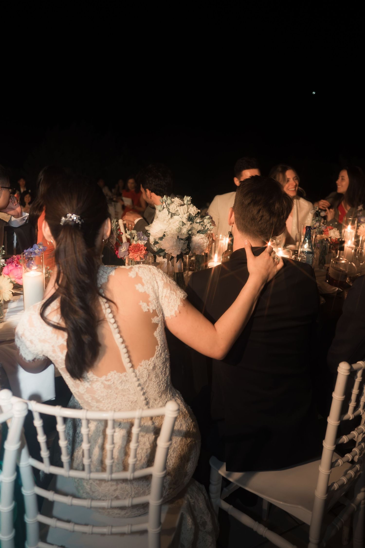 Bride in lace gown and groom share an intimate moment seated together at their candlelit reception.