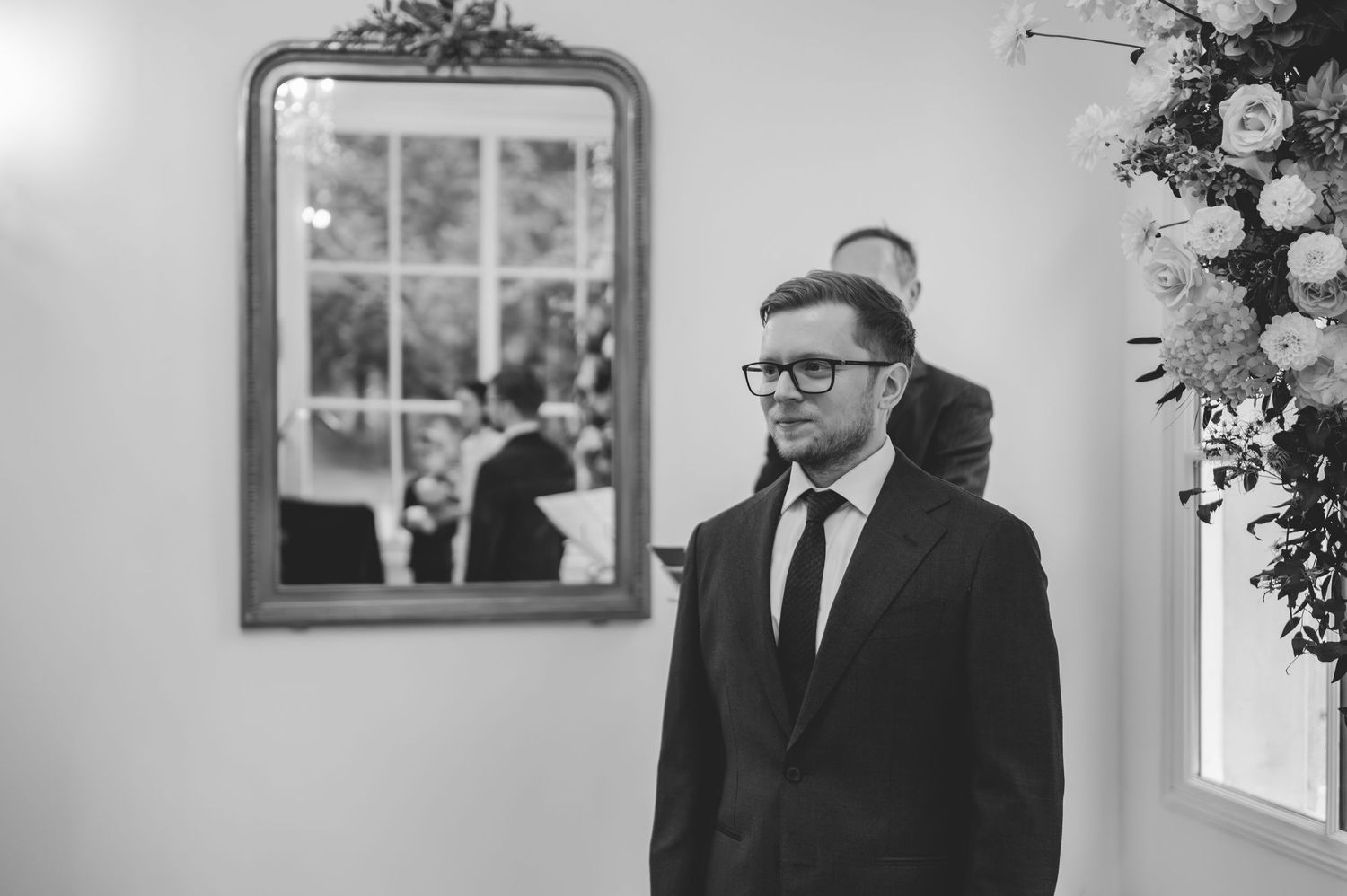 Groom in black suit waits nervously at the altar in black and white wedding ceremony photo.