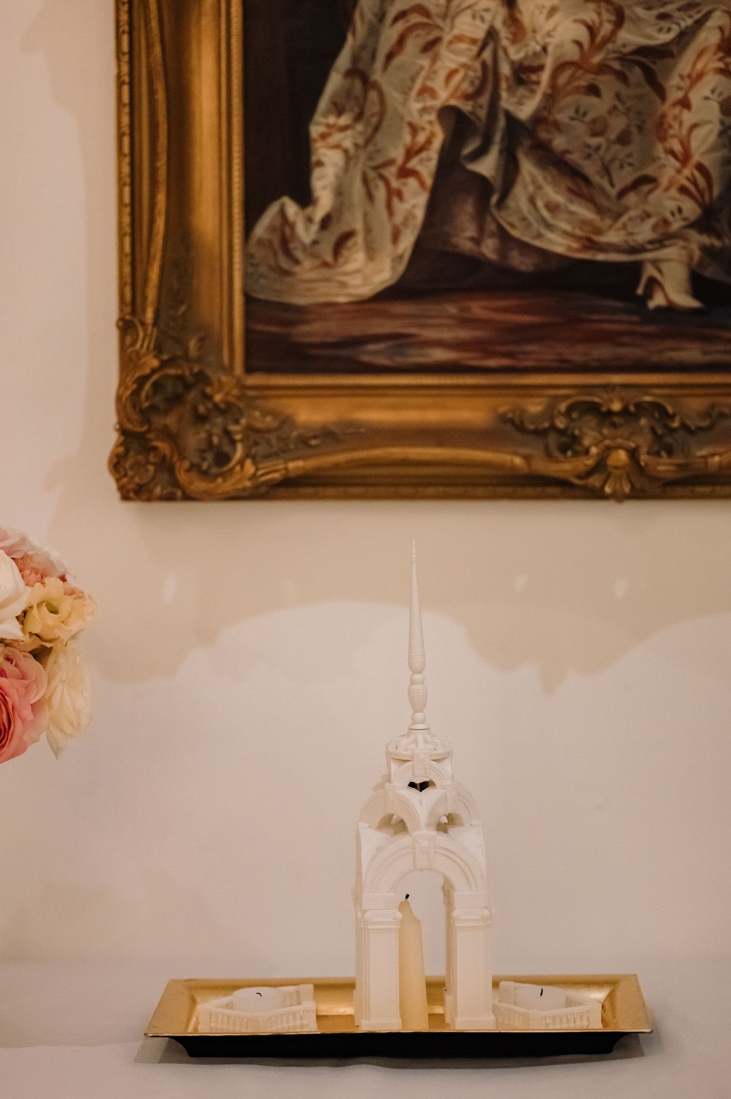 White ceramic church candle holder on gold tray beneath ornate framed painting.