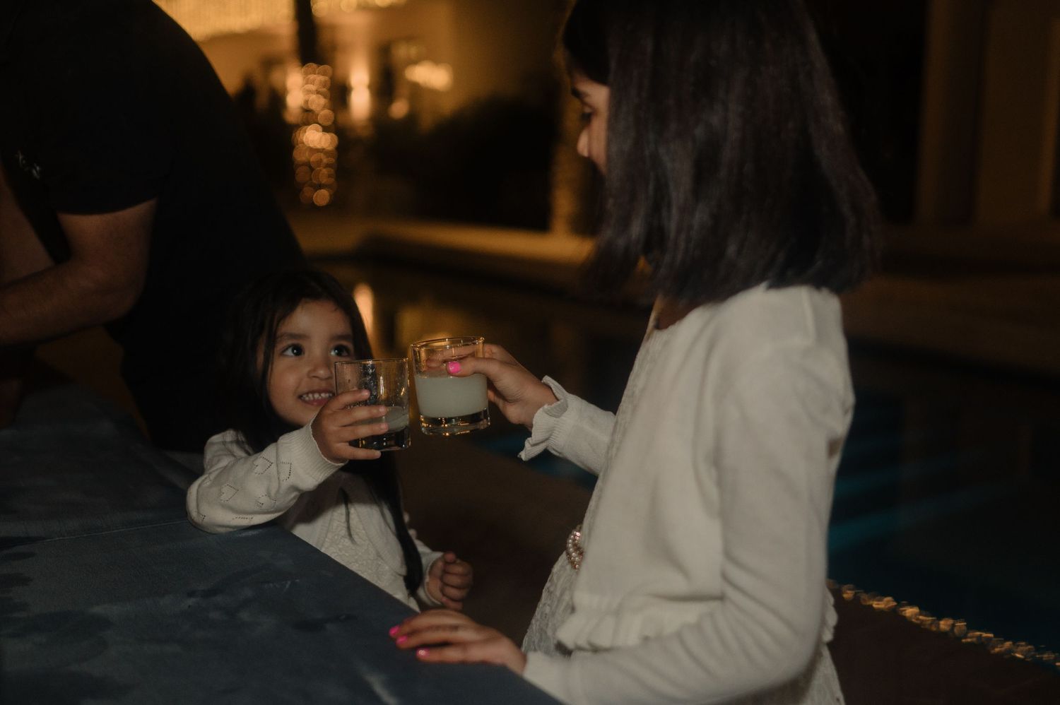 Two young girls clinking glasses together at a dimly lit celebration party.