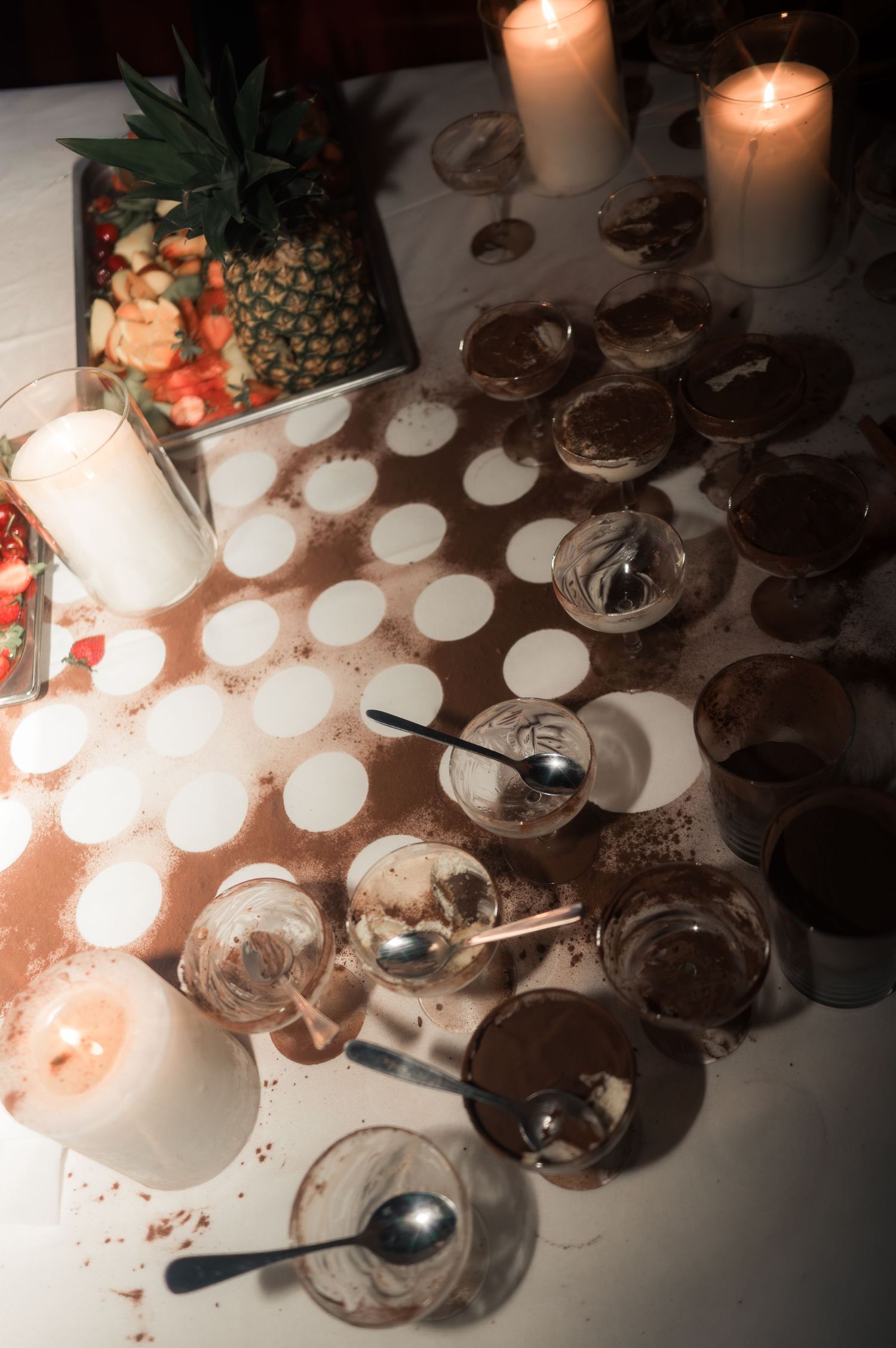 Empty dessert glasses with spoons and candles on a white tablecloth after a wedding reception.