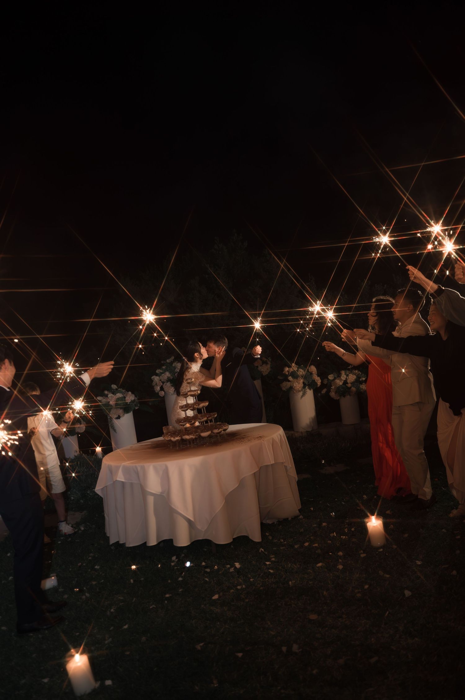 Wedding guests surrounding a cake table holding sparklers aloft in the dark night sky.