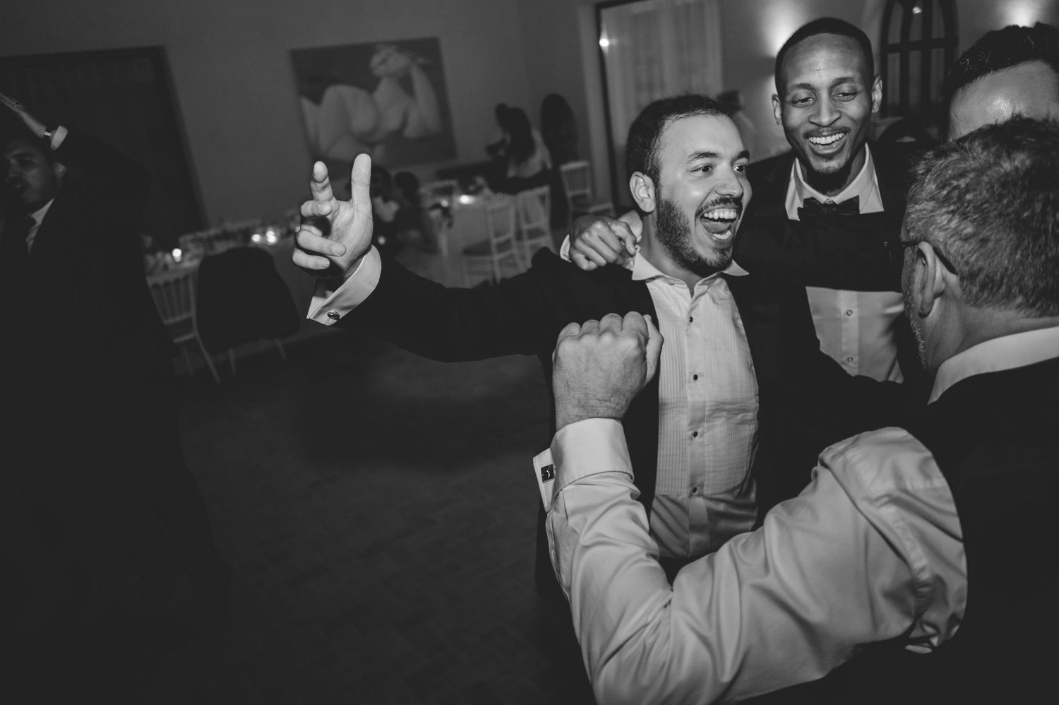 Black and white photo of men laughing and celebrating together on wedding reception dance floor.