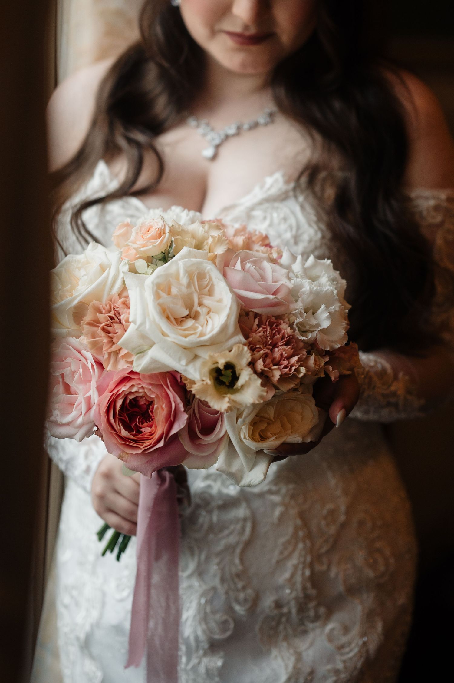 Close-up of a bridal bouquet featuring pink roses, peonies, and white flowers with ribbon.