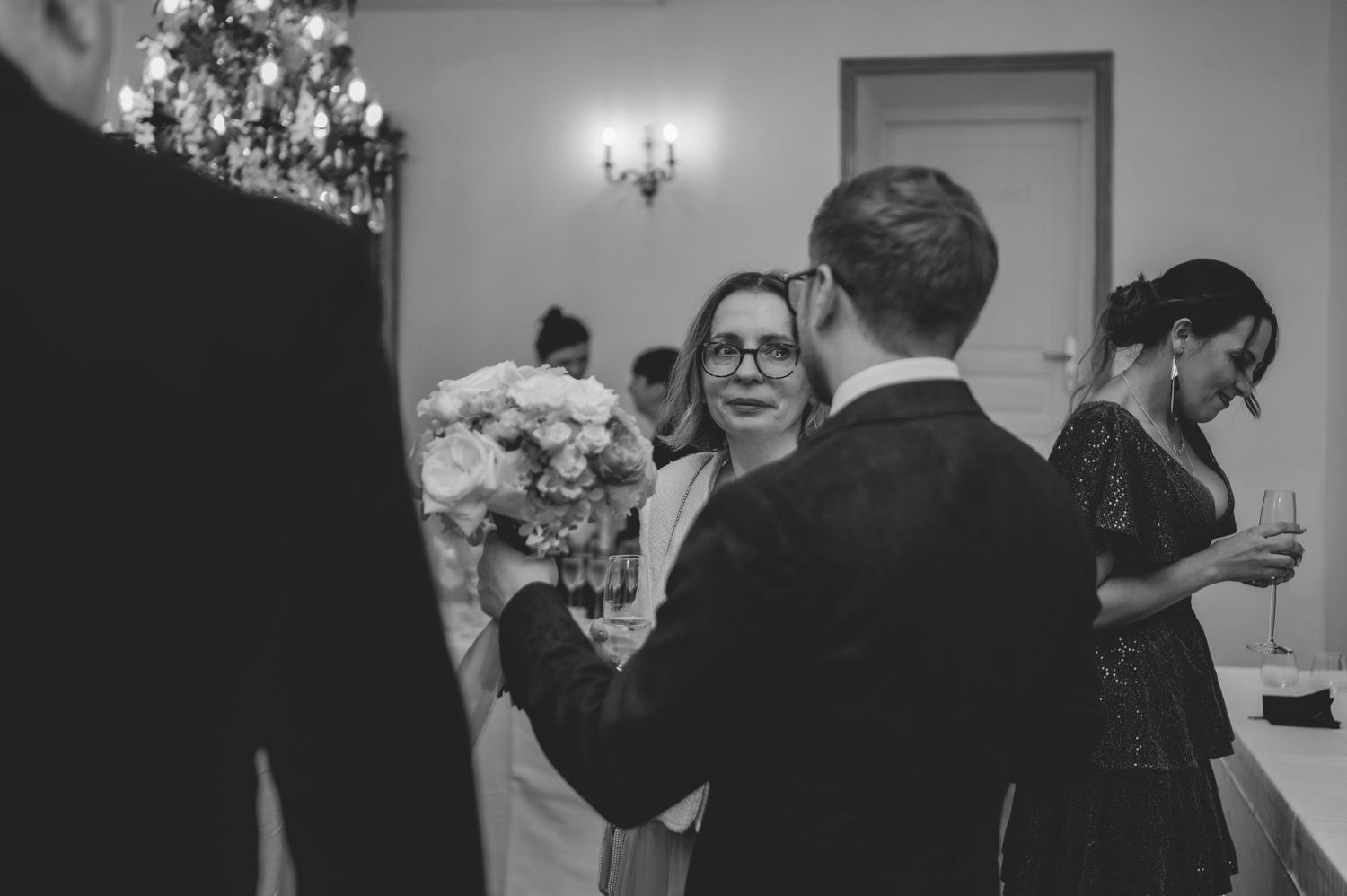 Black and white wedding reception photo of guests mingling with floral centerpiece in background.