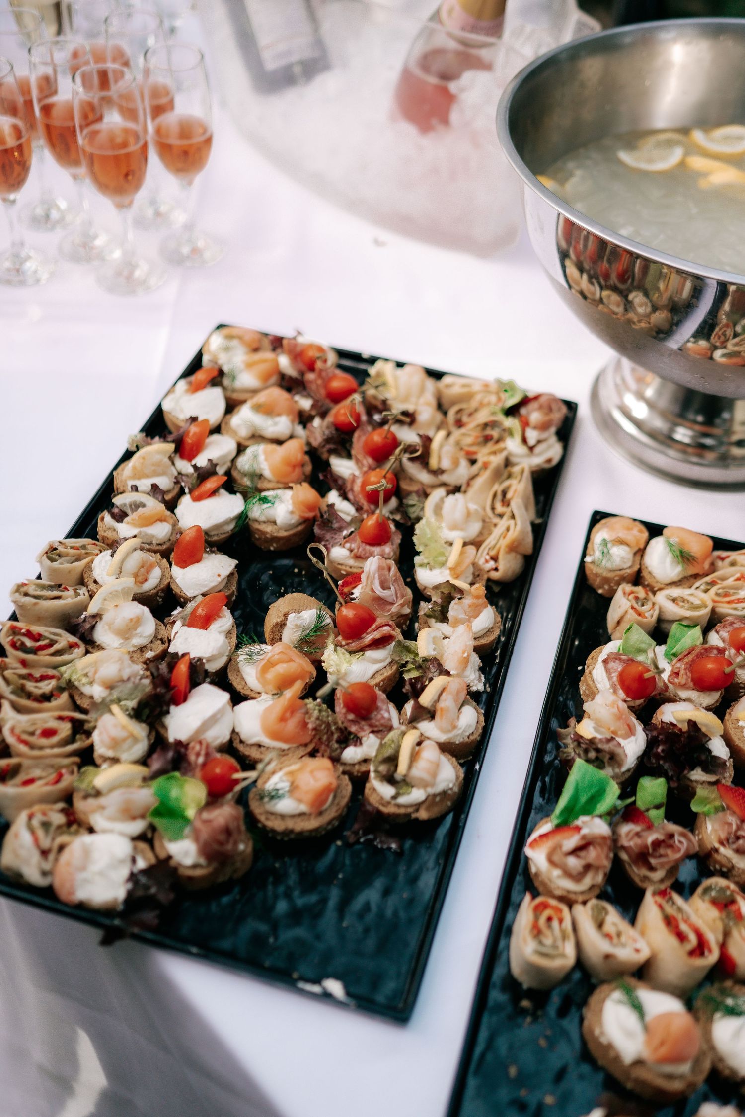Elegant wedding canapé display with assorted bite-sized appetizers and champagne glasses on white tablecloth.