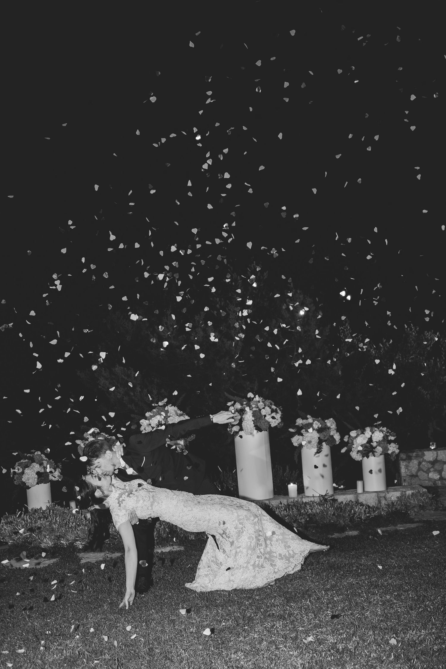 Bride being dipped surrounded by falling flower petals at outdoor night wedding in black and white.