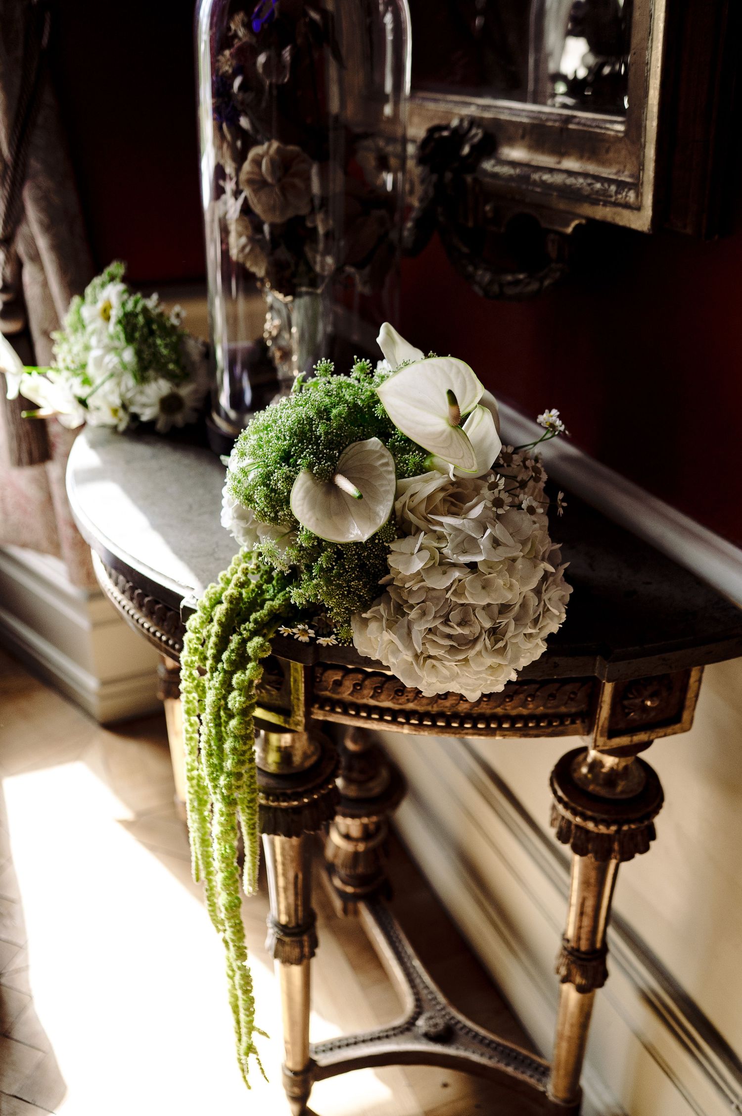 Elegant bridal bouquet with white calla lilies, hydrangeas, and cascading green amaranthus on antique table.