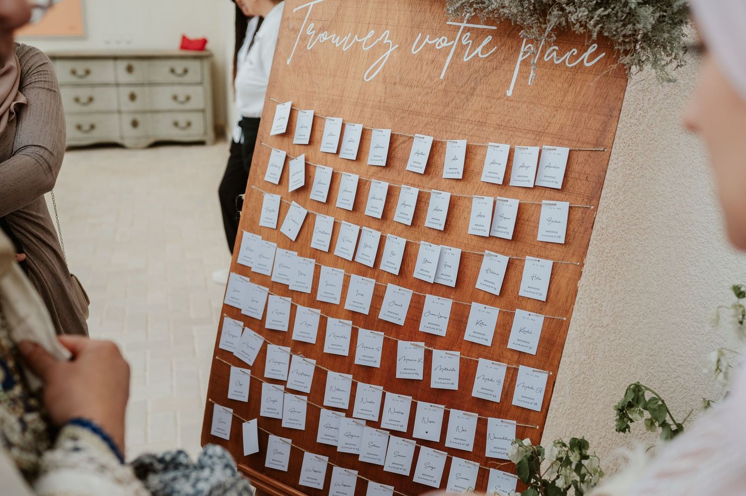 Wooden seating chart board with white card holders and cursive text at wedding reception.