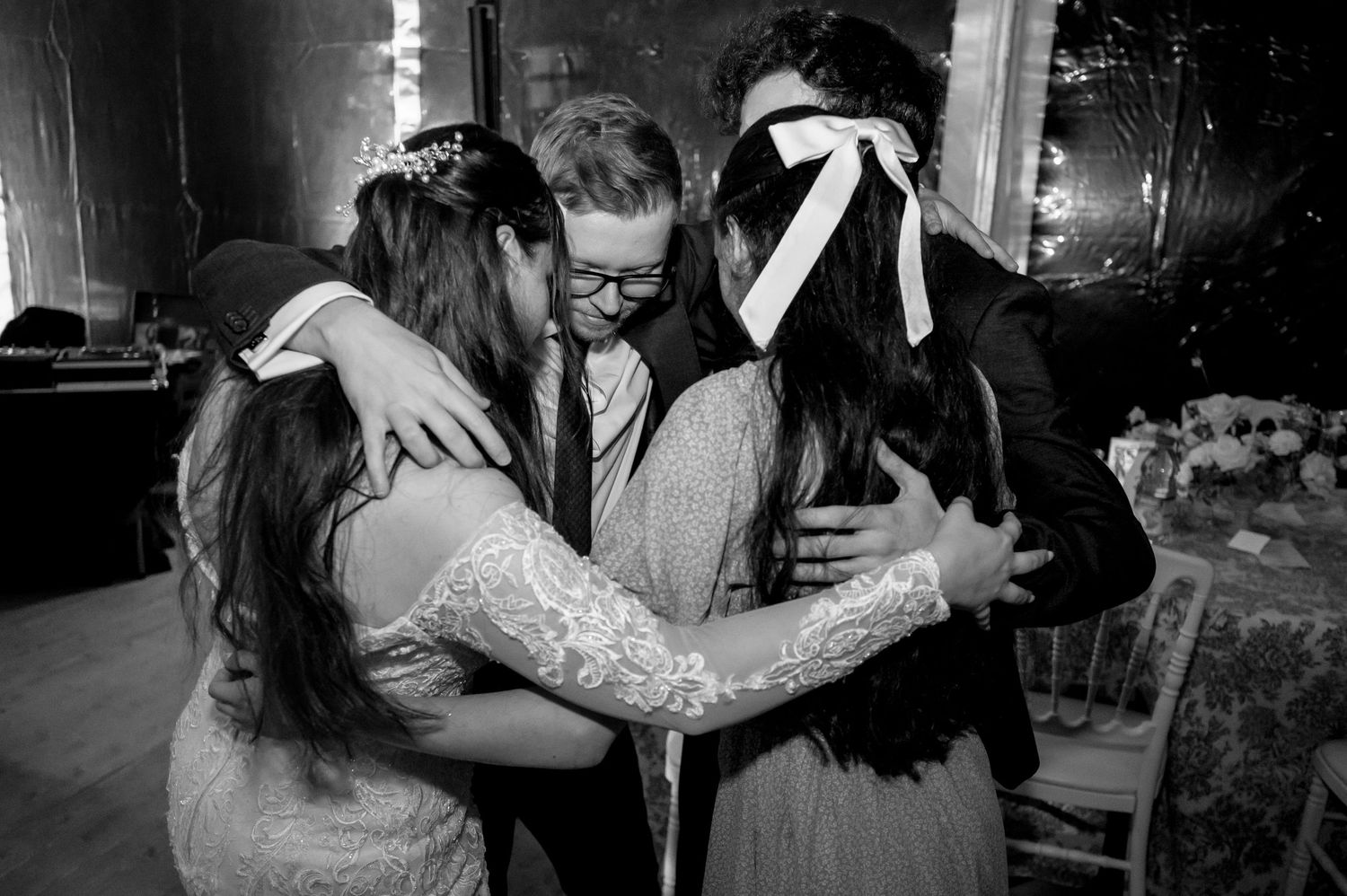 Bride, groom, and guest share warm group hug at wedding reception in black and white.