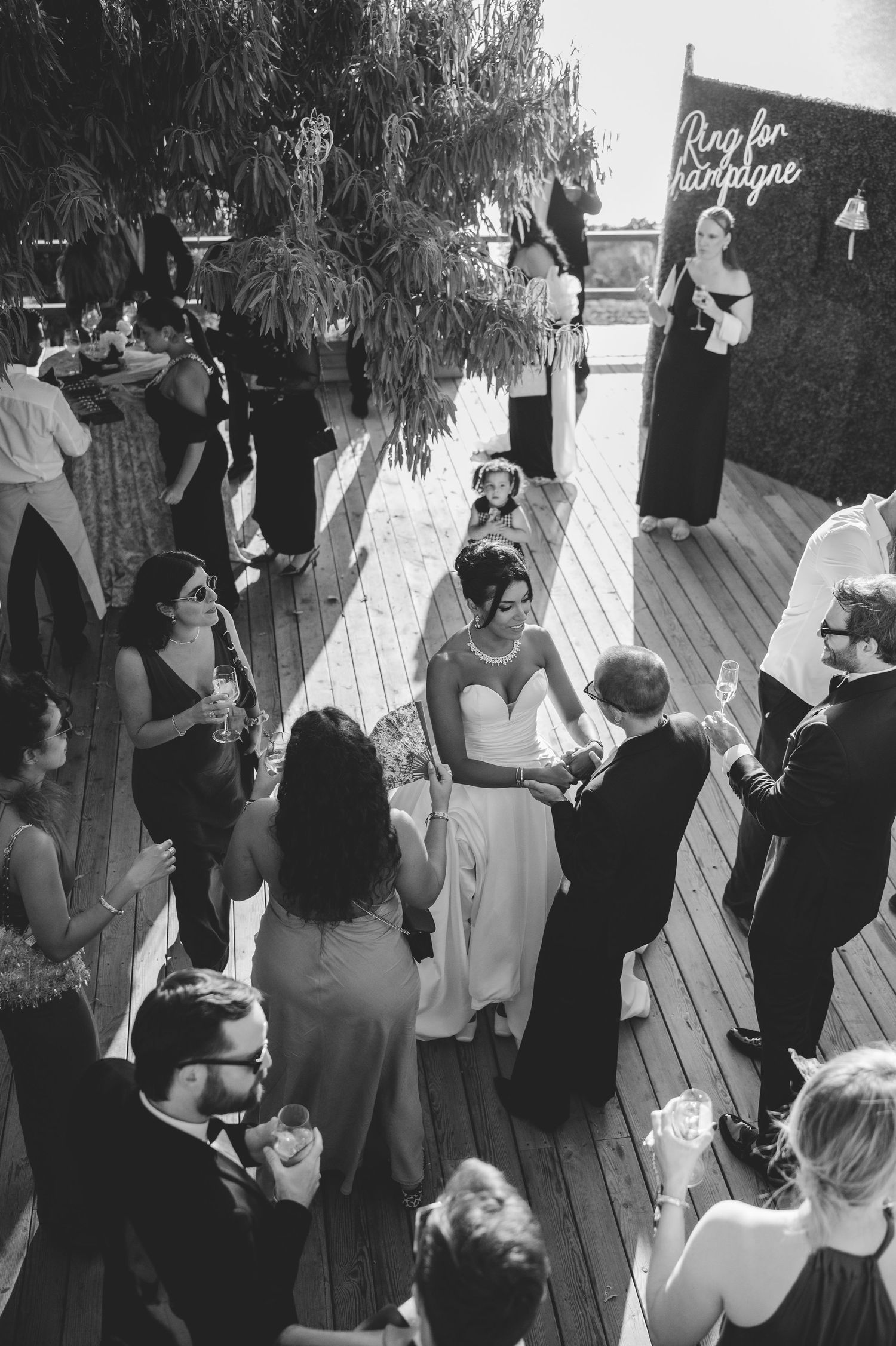 Aerial black and white view of bride and groom dancing surrounded by wedding guests on deck.