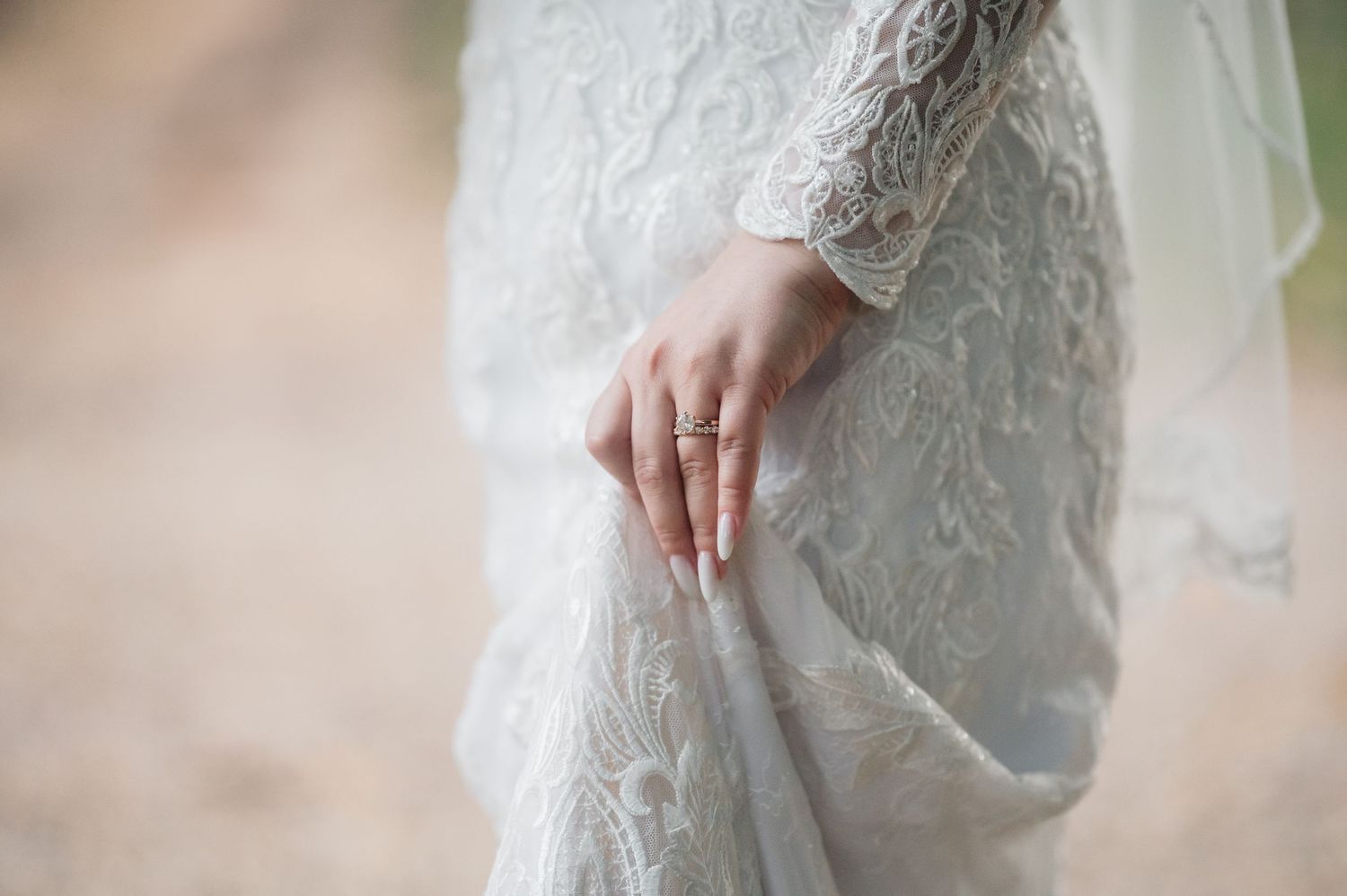 Close-up of bride's hand wearing wedding ring, holding lace wedding gown hem delicately.