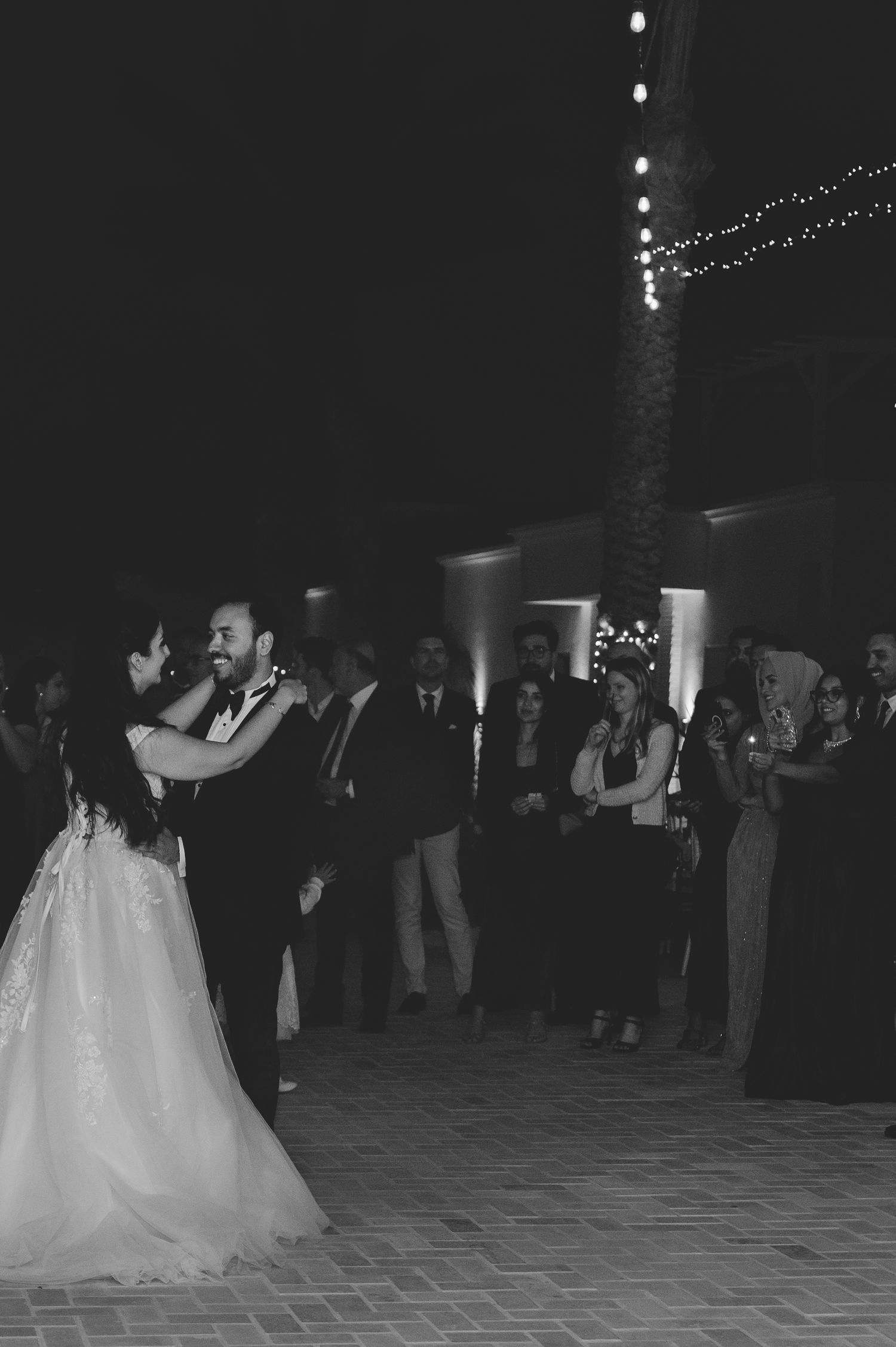 Bride and groom share romantic first dance outdoors under string lights at night reception.