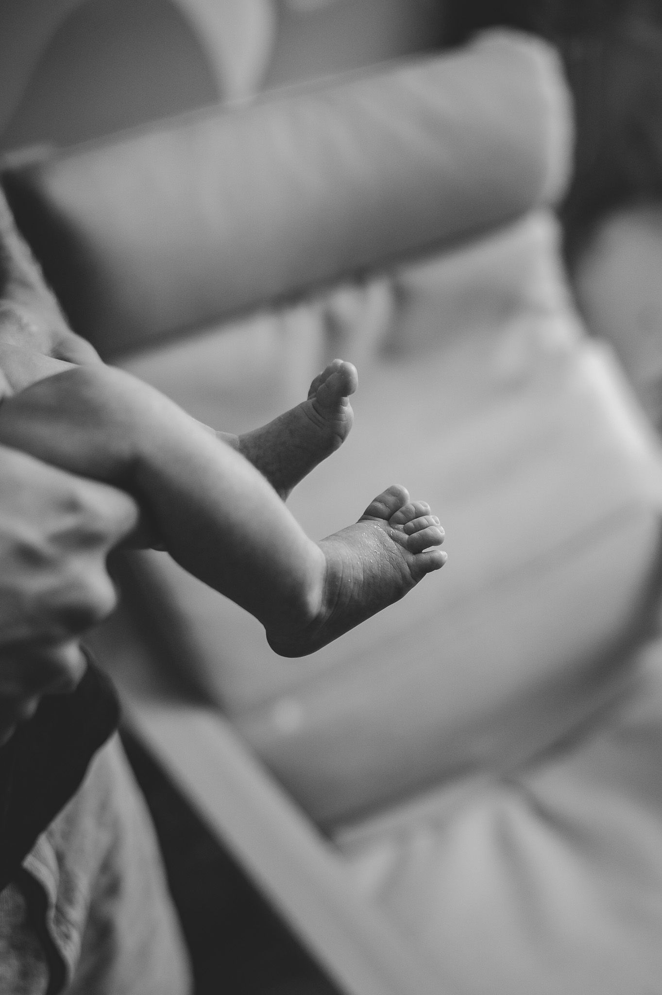 Black and white close-up of tiny newborn baby feet resting on a soft blanket.