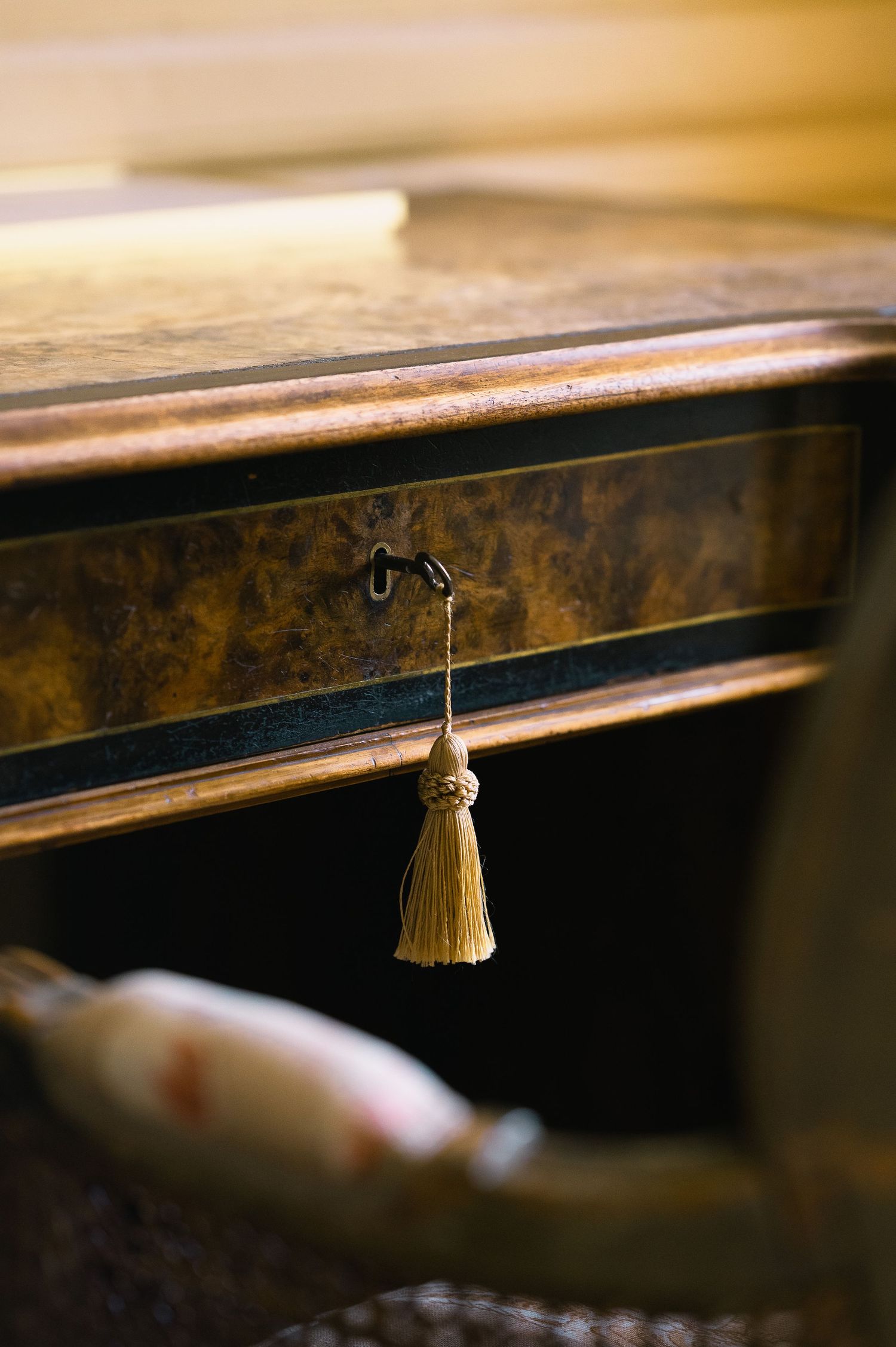 Antique wooden desk drawer with ornate gold tassel key in warm bokeh light.