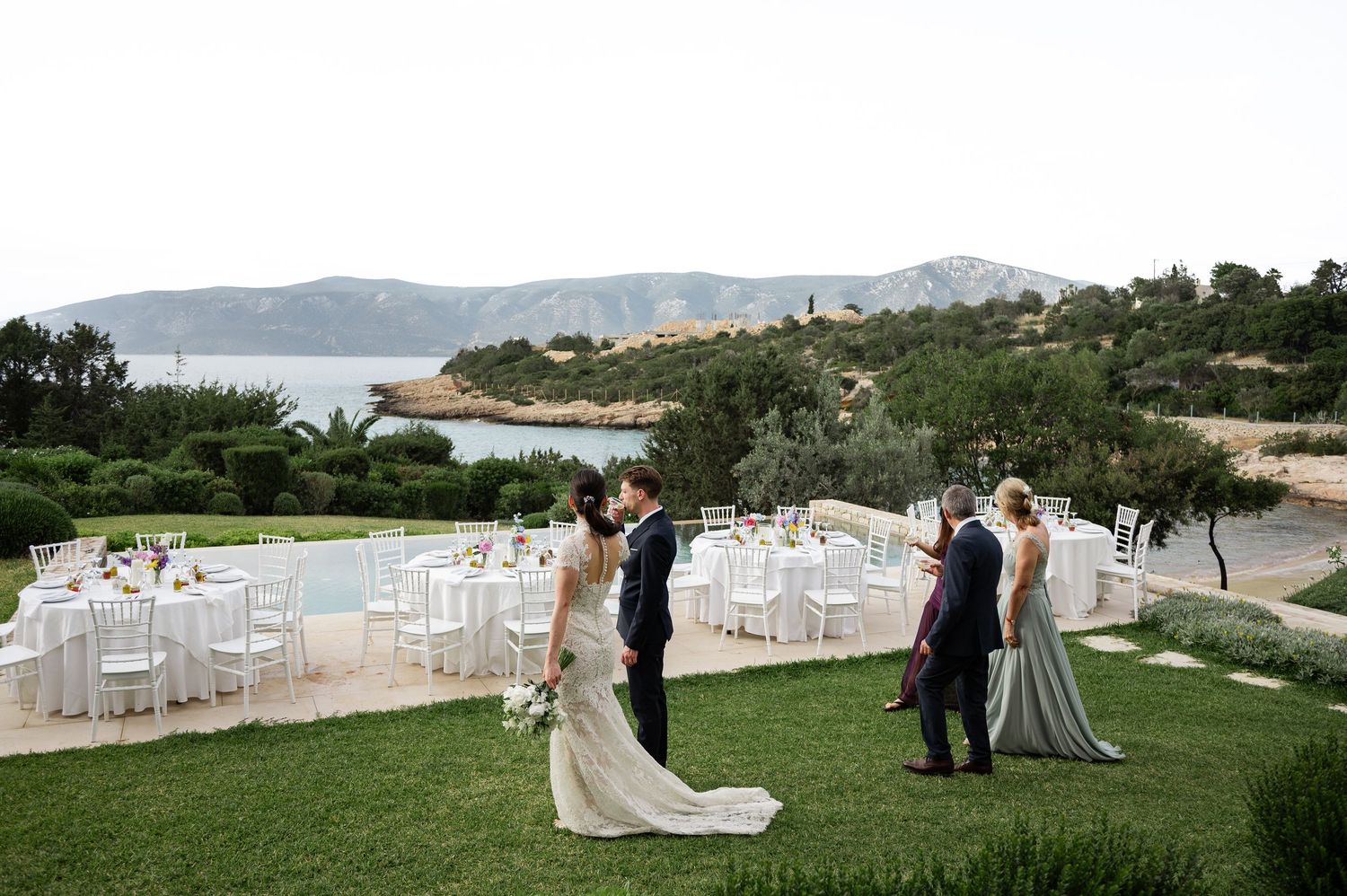 Newlyweds survey elegant outdoor wedding reception venue overlooking scenic Mediterranean coastline.