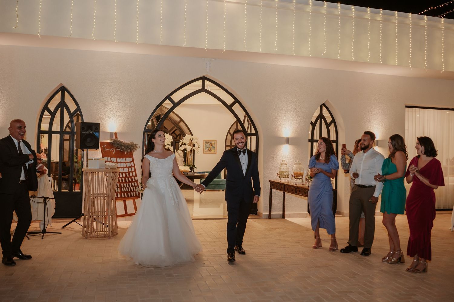Bride and groom make grand entrance holding hands at elegant wedding reception venue.