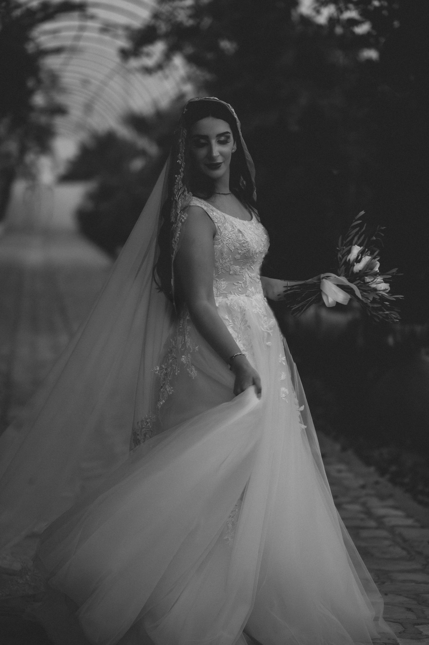 Black and white portrait of bride in flowing tulle gown and lace veil holding a bridal bouquet.