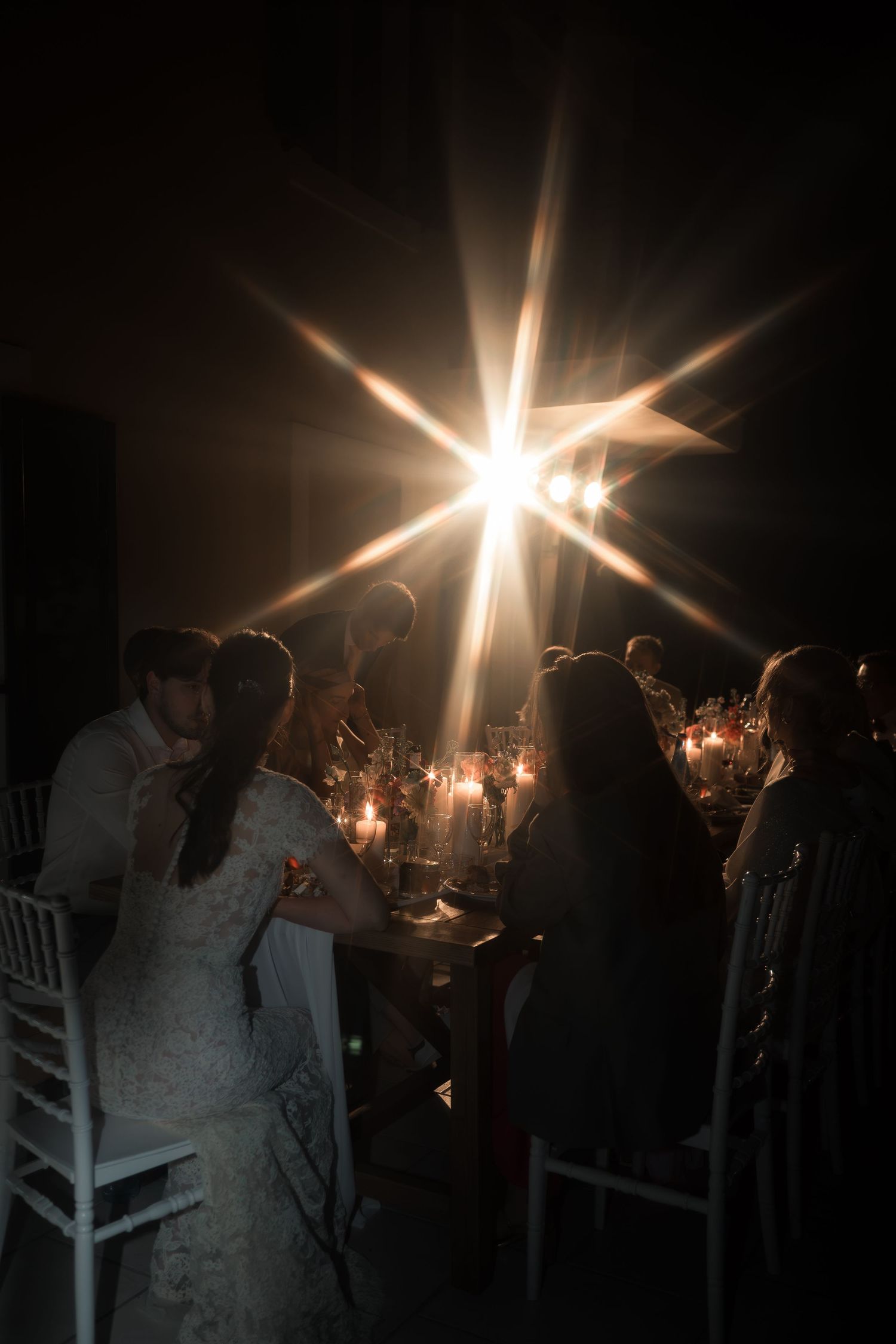 Bride and groom sit at a candlelit wedding reception table beneath a dramatic starburst light effect.