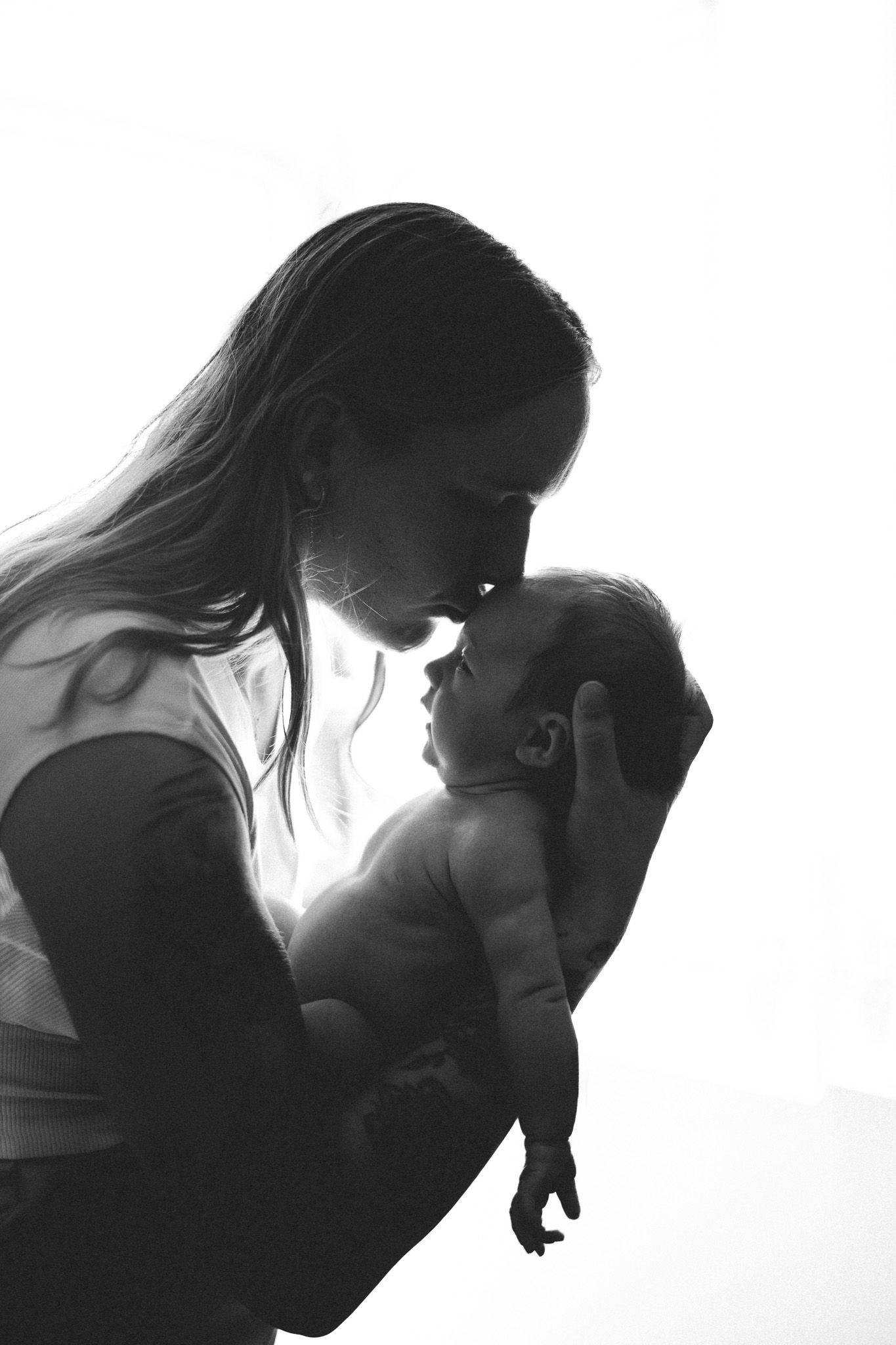 Black and white silhouette of a mother tenderly holding her newborn baby face to face against white background.