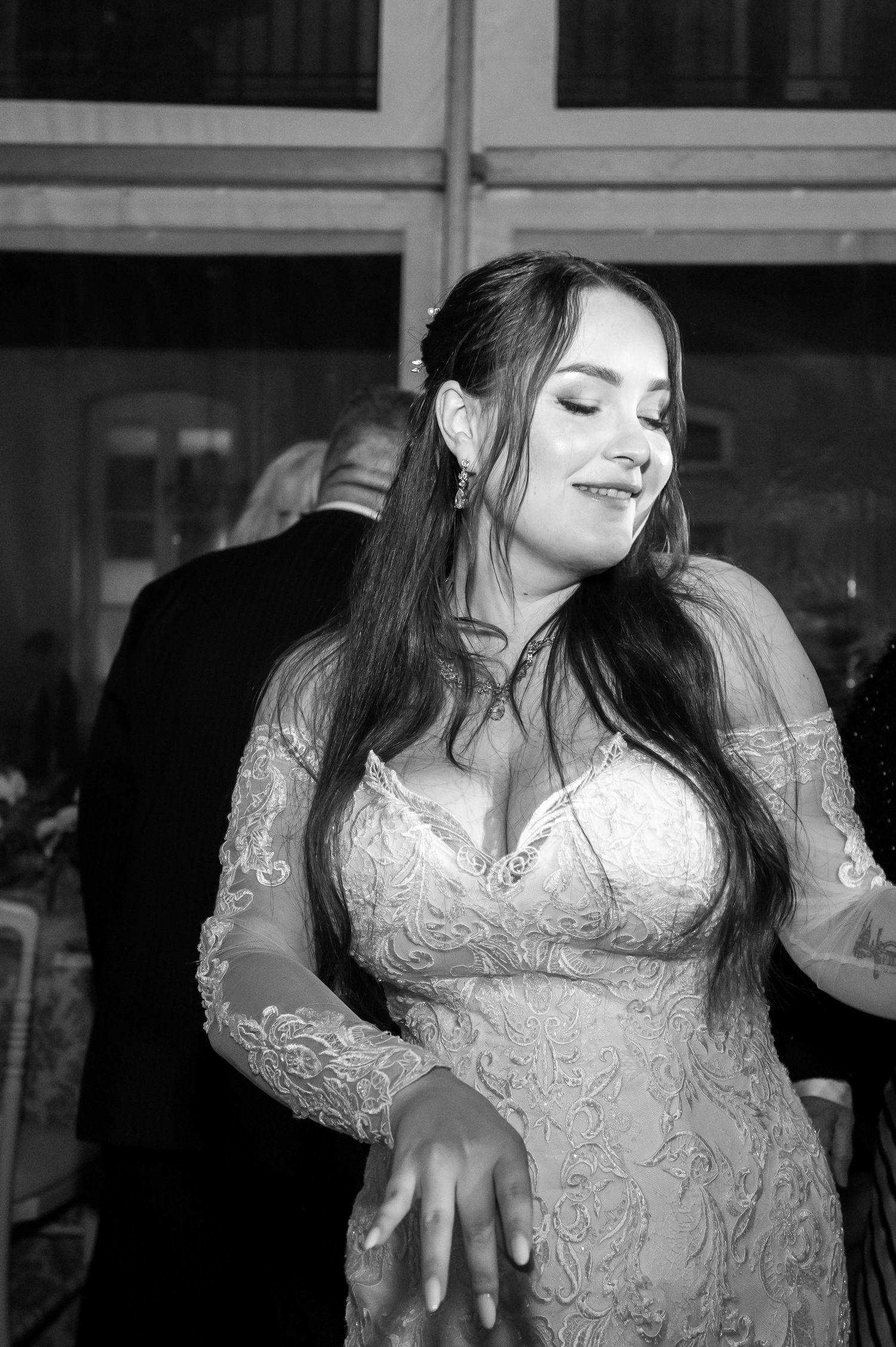Bride in lace wedding gown poses elegantly in black and white photo.