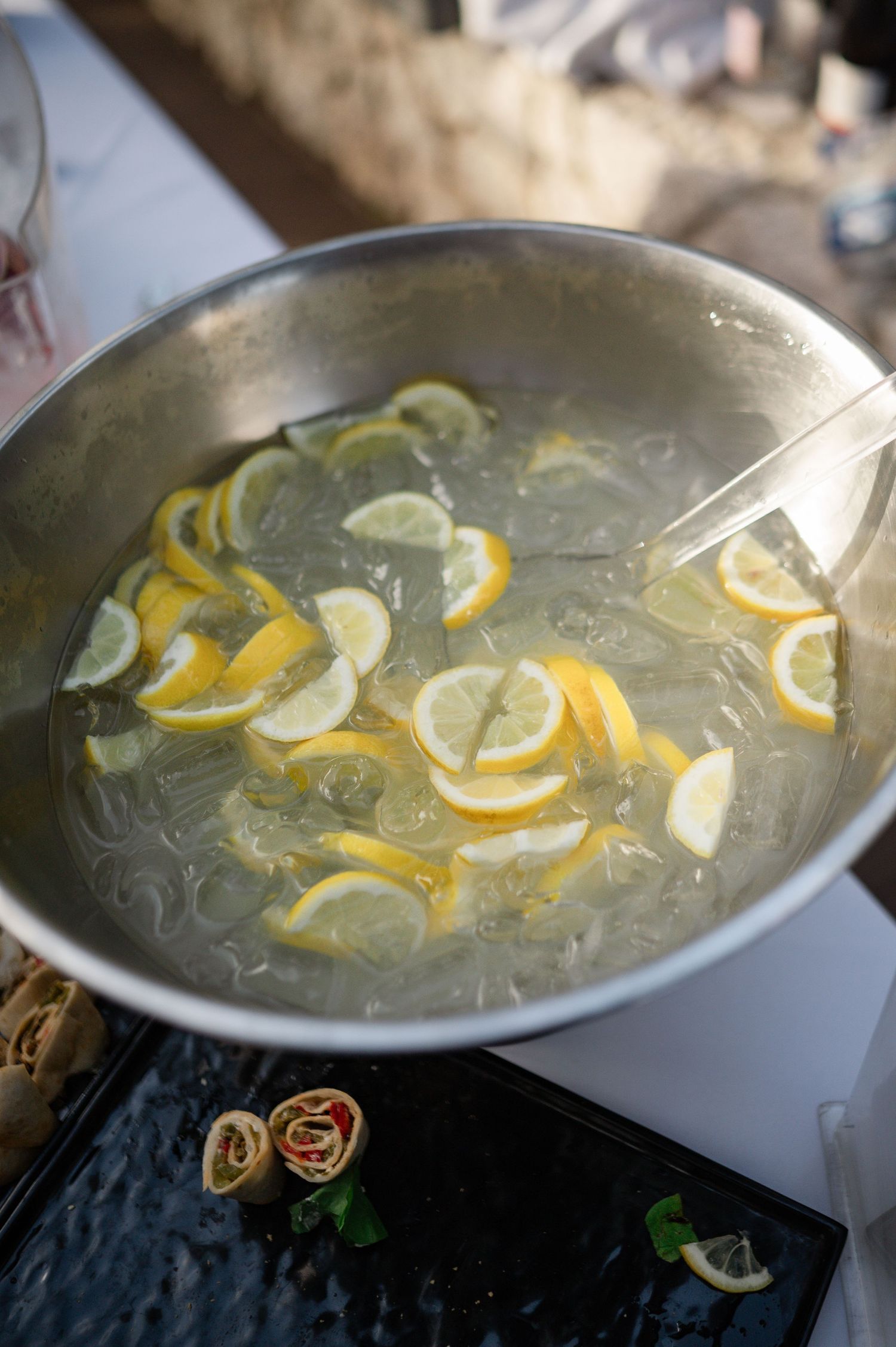 Large punch bowl filled with lemon and lime slices served at an outdoor wedding reception.