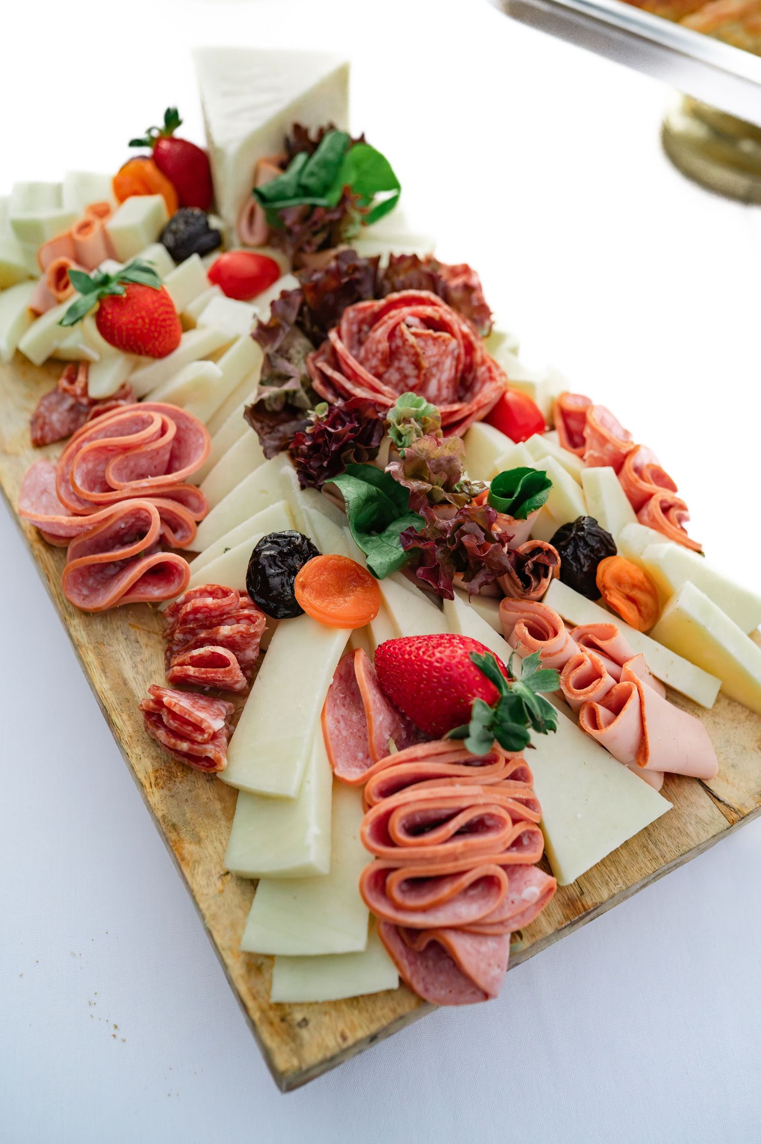 Elegant charcuterie board with rolled meats, cheese slices, strawberries and garnishes.