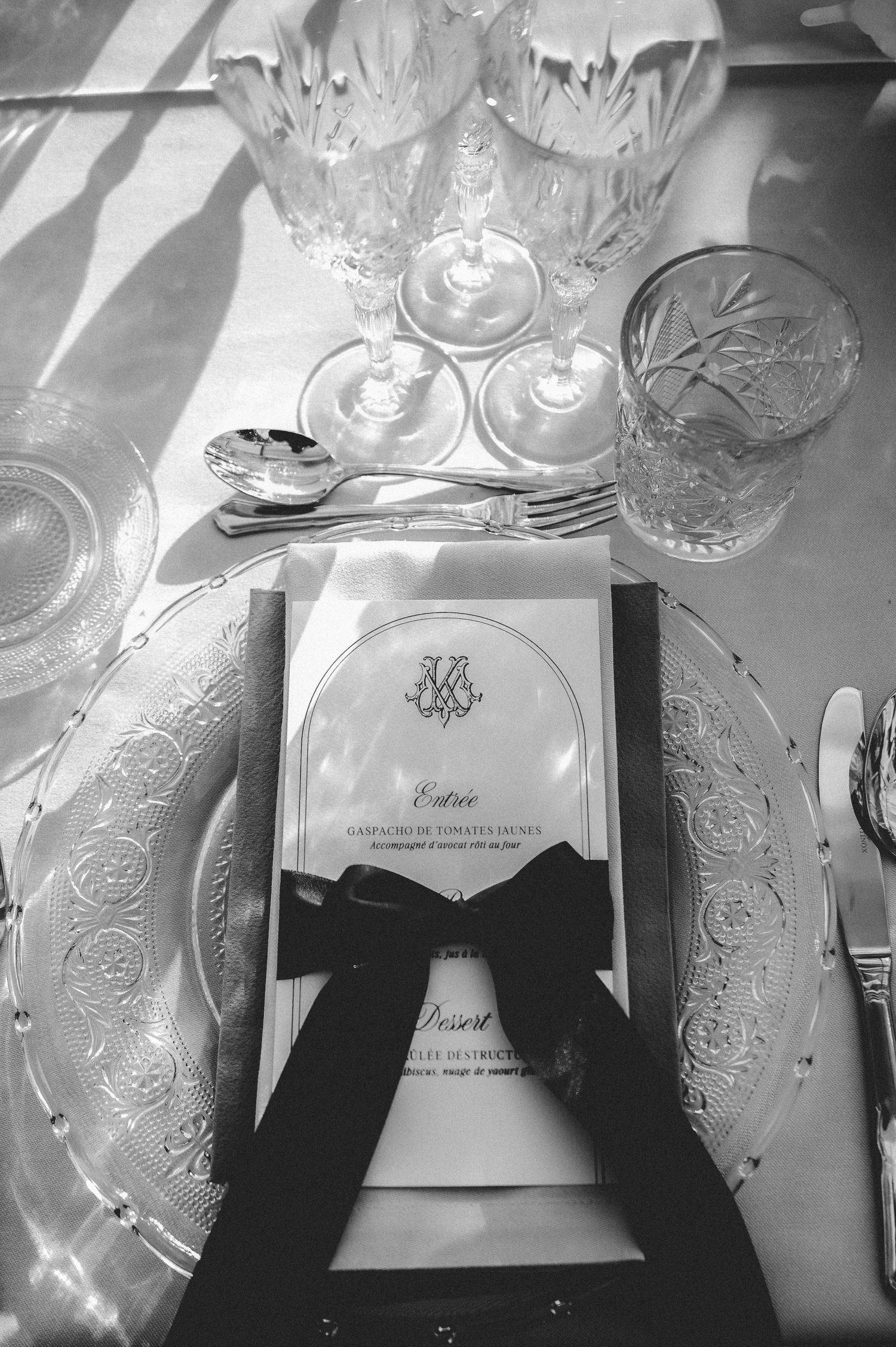 Black and white wedding table setting with crystal glassware, monogrammed menu card tied with dark ribbon on charger plate.