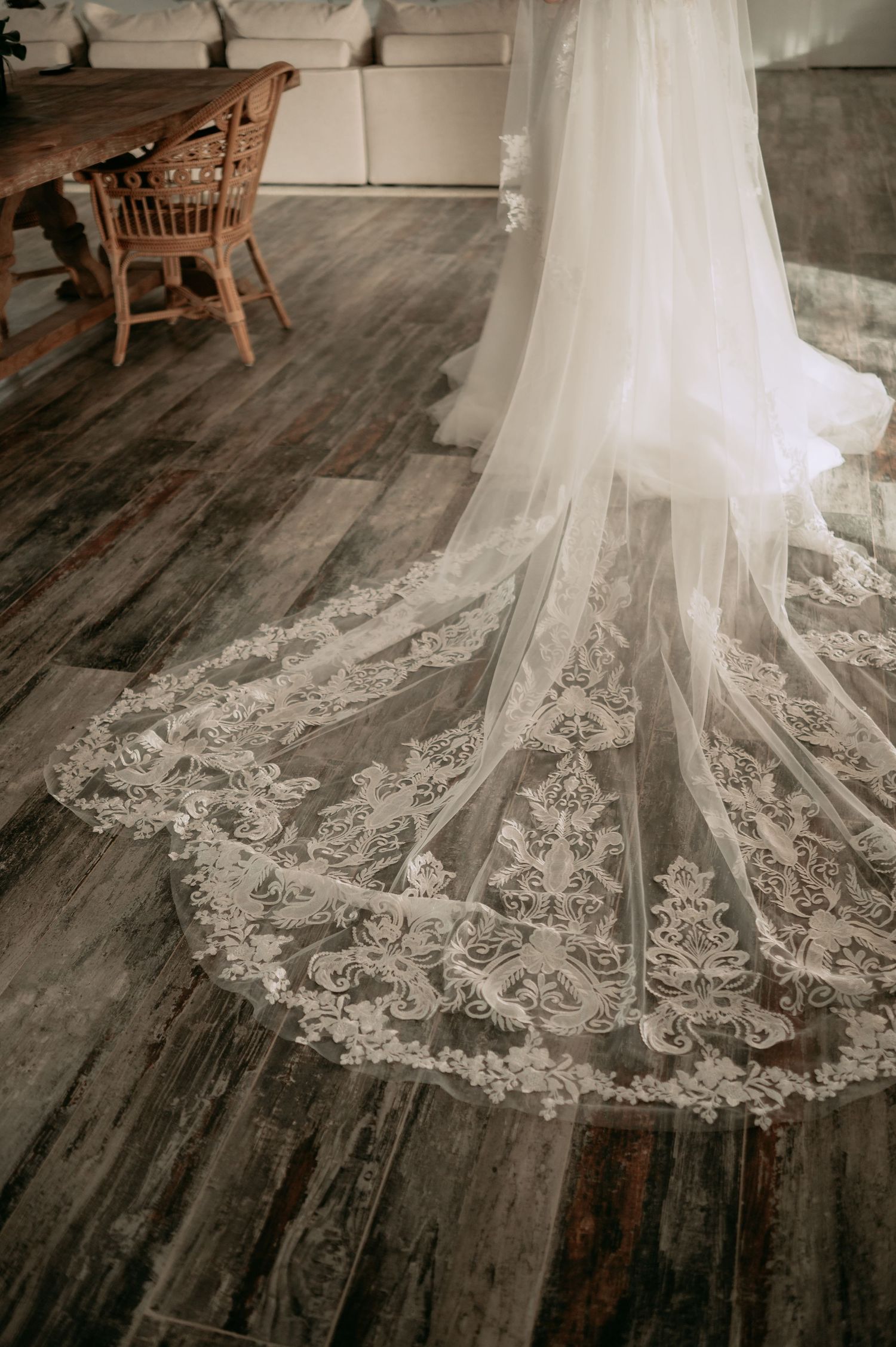 Detailed lace cathedral wedding veil train spread on rustic hardwood floor.