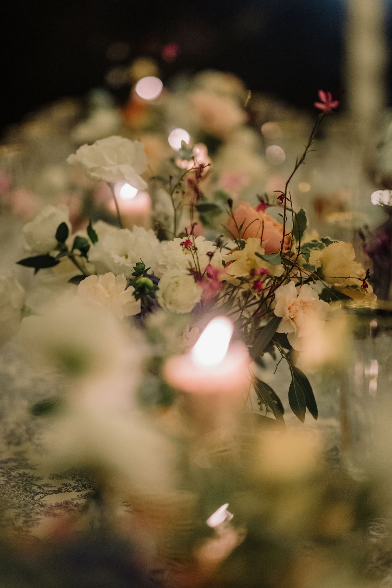 Close-up of romantic wedding table centerpiece with white and pink flowers surrounded by glowing candles.