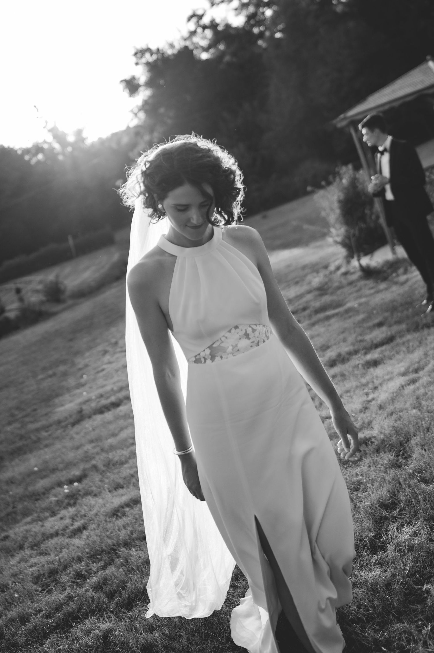 Bride in halter neck gown with veil smiles softly in black and white garden photo.
