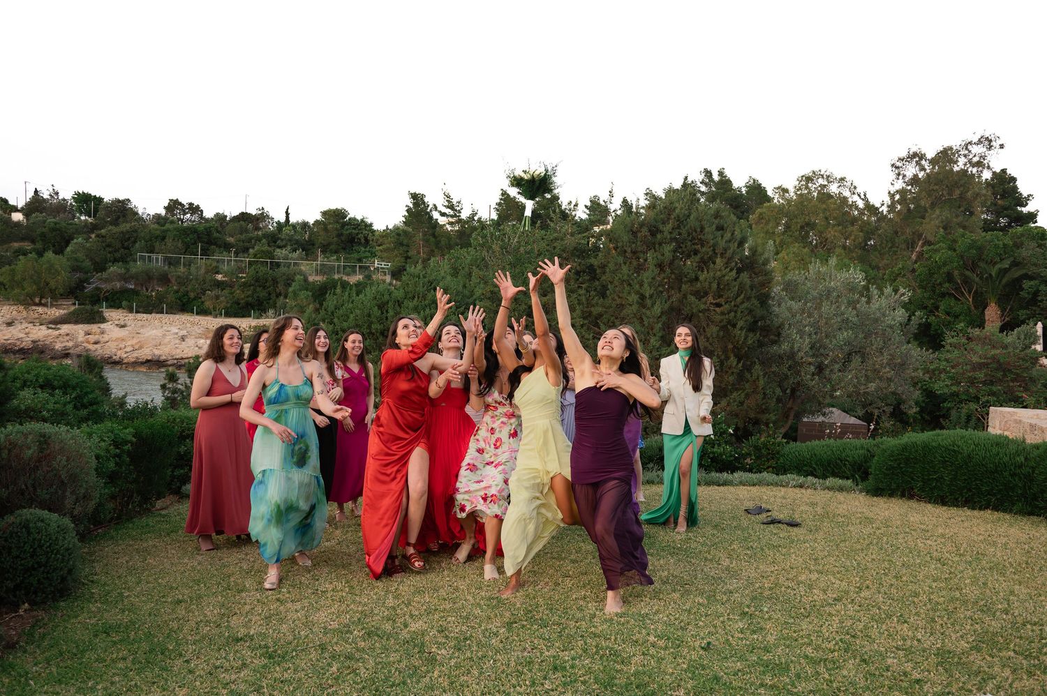 Joyful group of bridesmaids in colorful dresses celebrating and dancing outdoors at garden wedding.