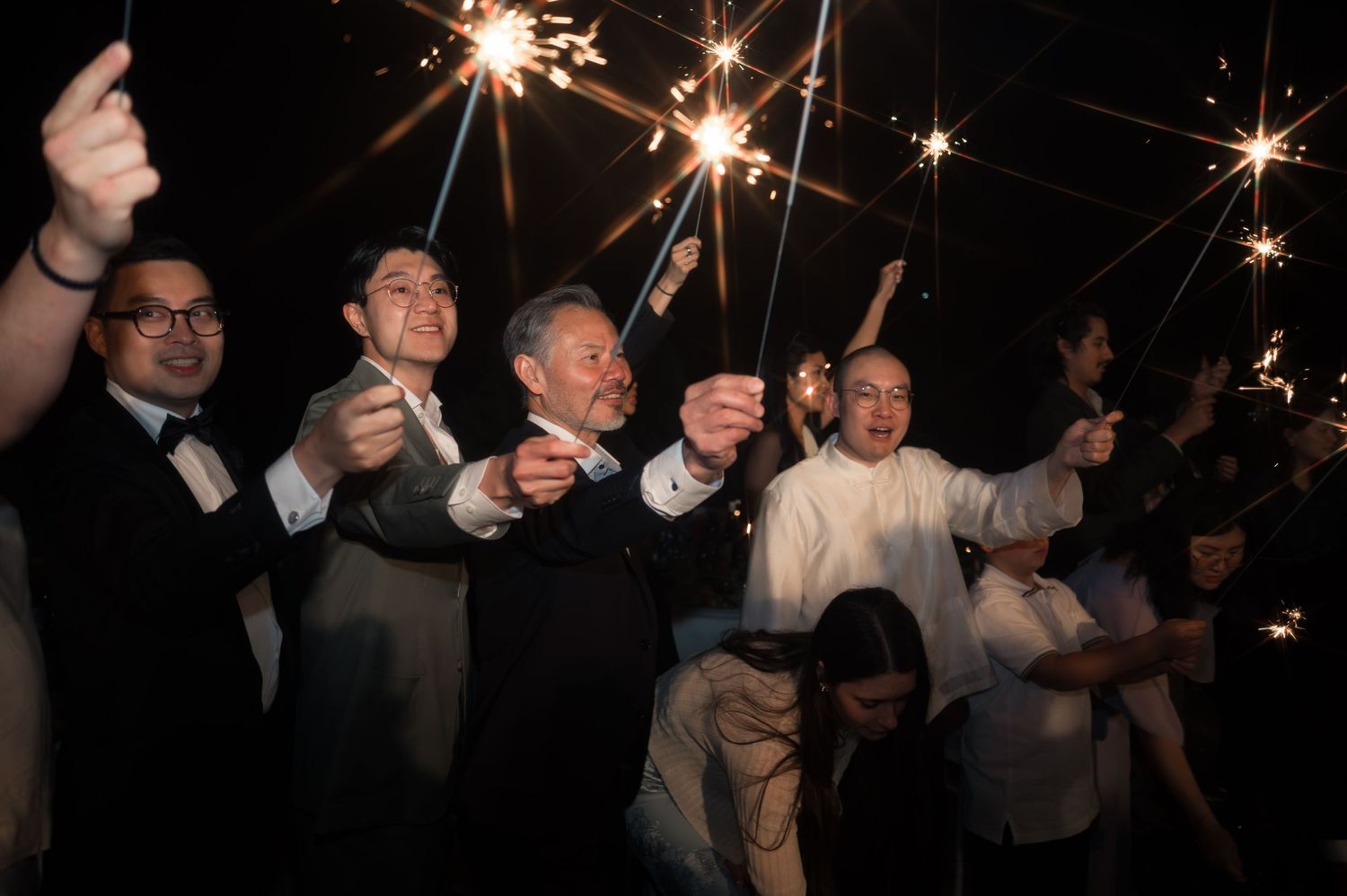 Wedding guests smiling and holding sparklers during a nighttime outdoor celebration.