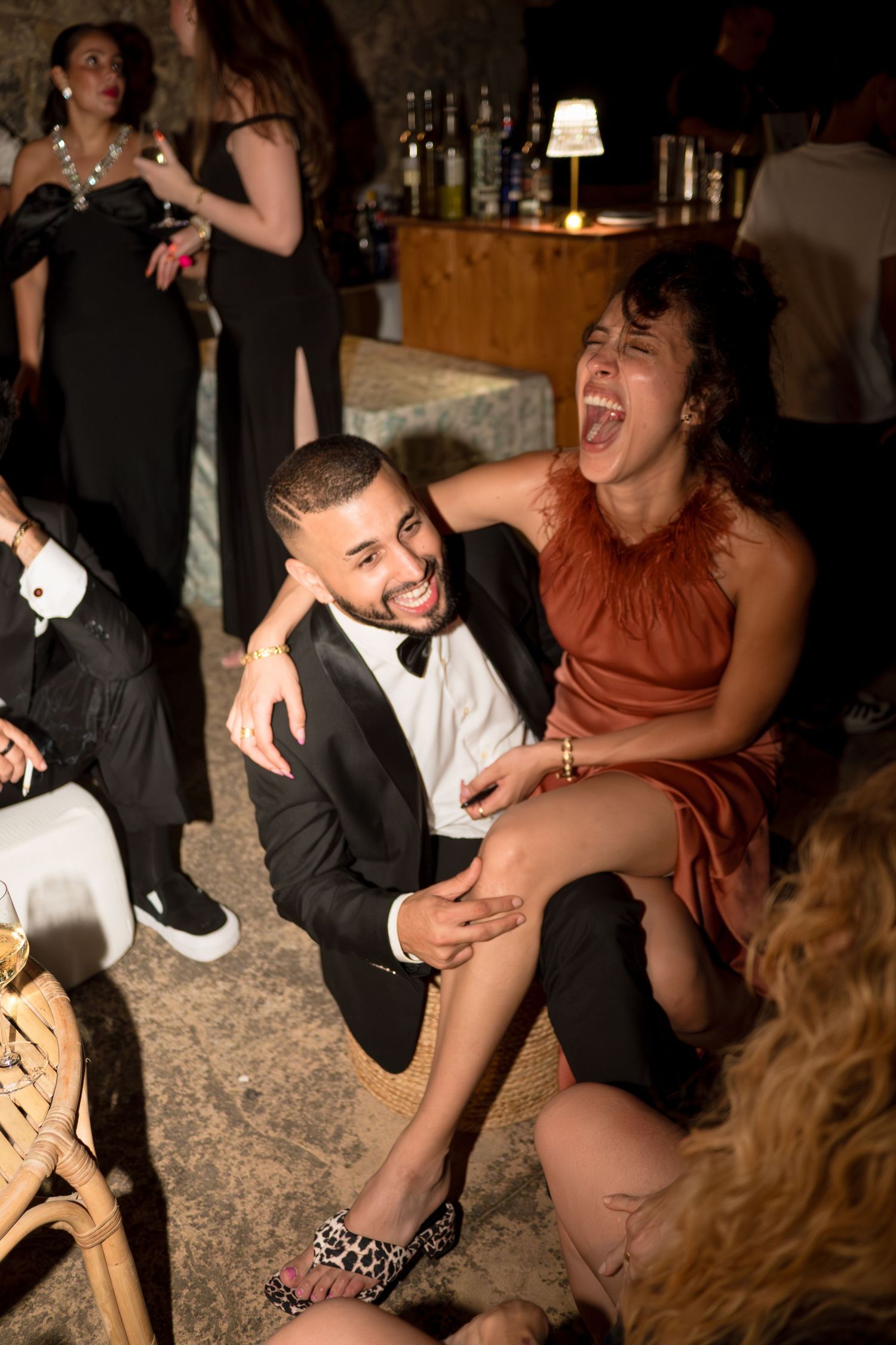 Couple laughing joyfully together at a wedding reception party in a dimly lit venue.