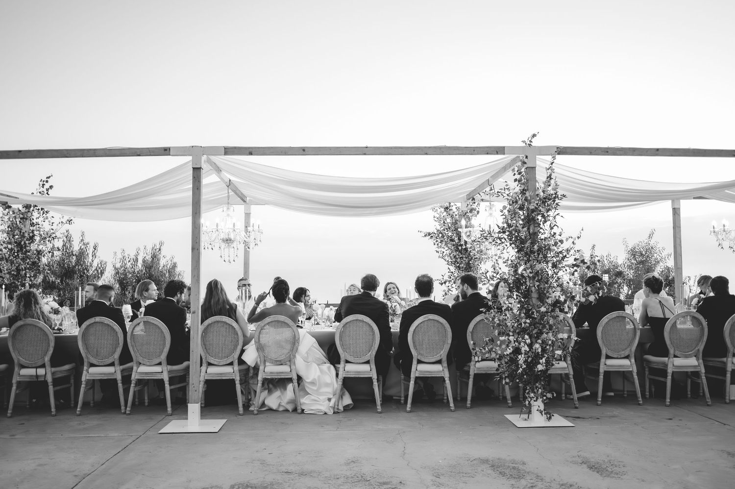 Elegant outdoor wedding reception with long dining table under draped white canopy with mountain views.