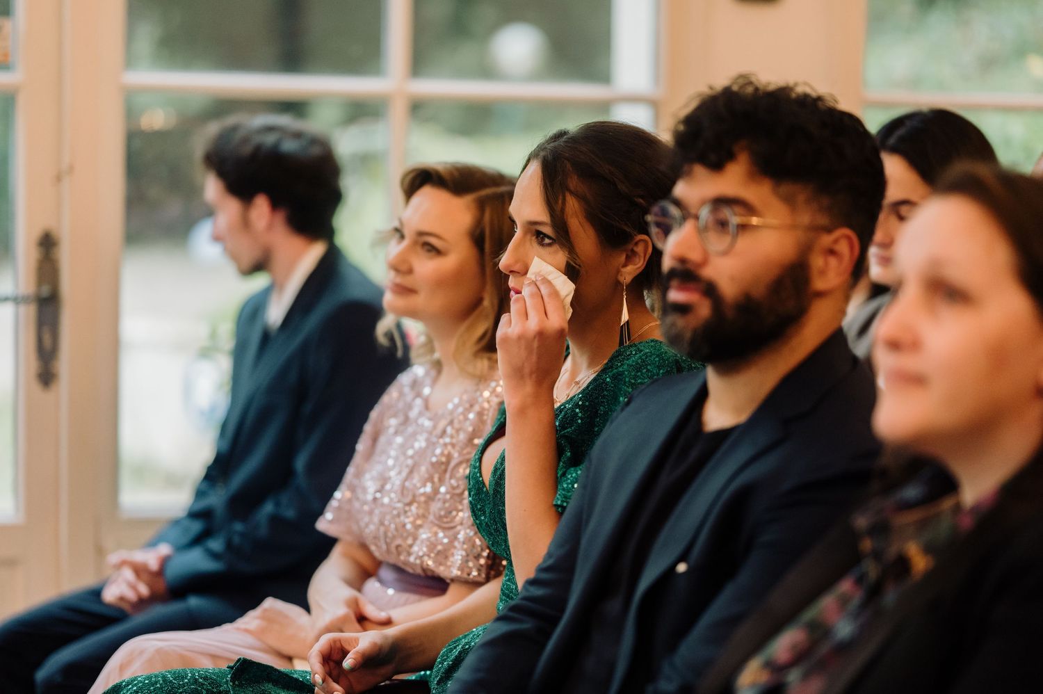 Emotional wedding guests seated in rows, with a woman wiping tears during the ceremony.