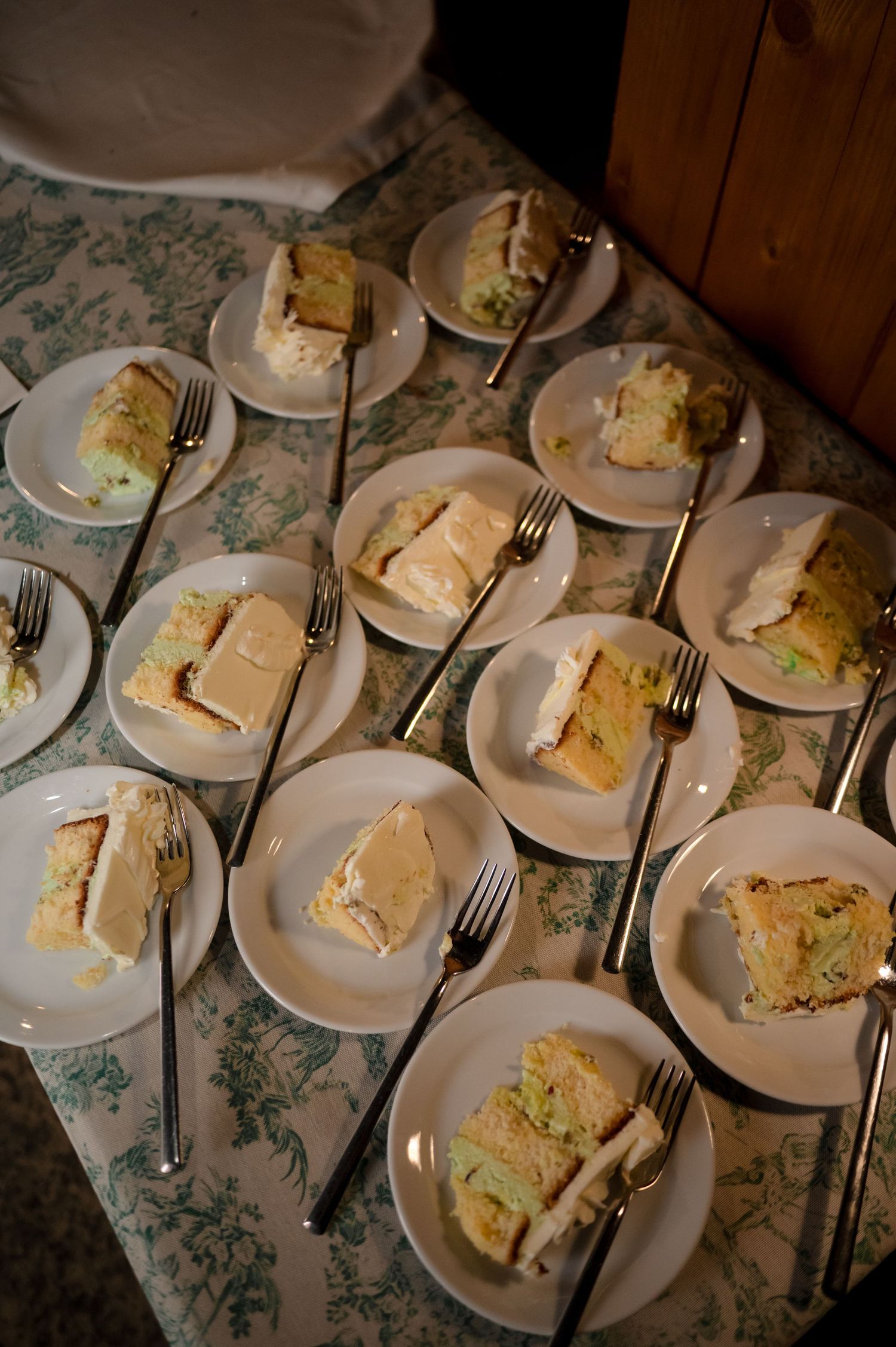 Neatly arranged slices of white wedding cake served on plates with forks on floral tablecloth.