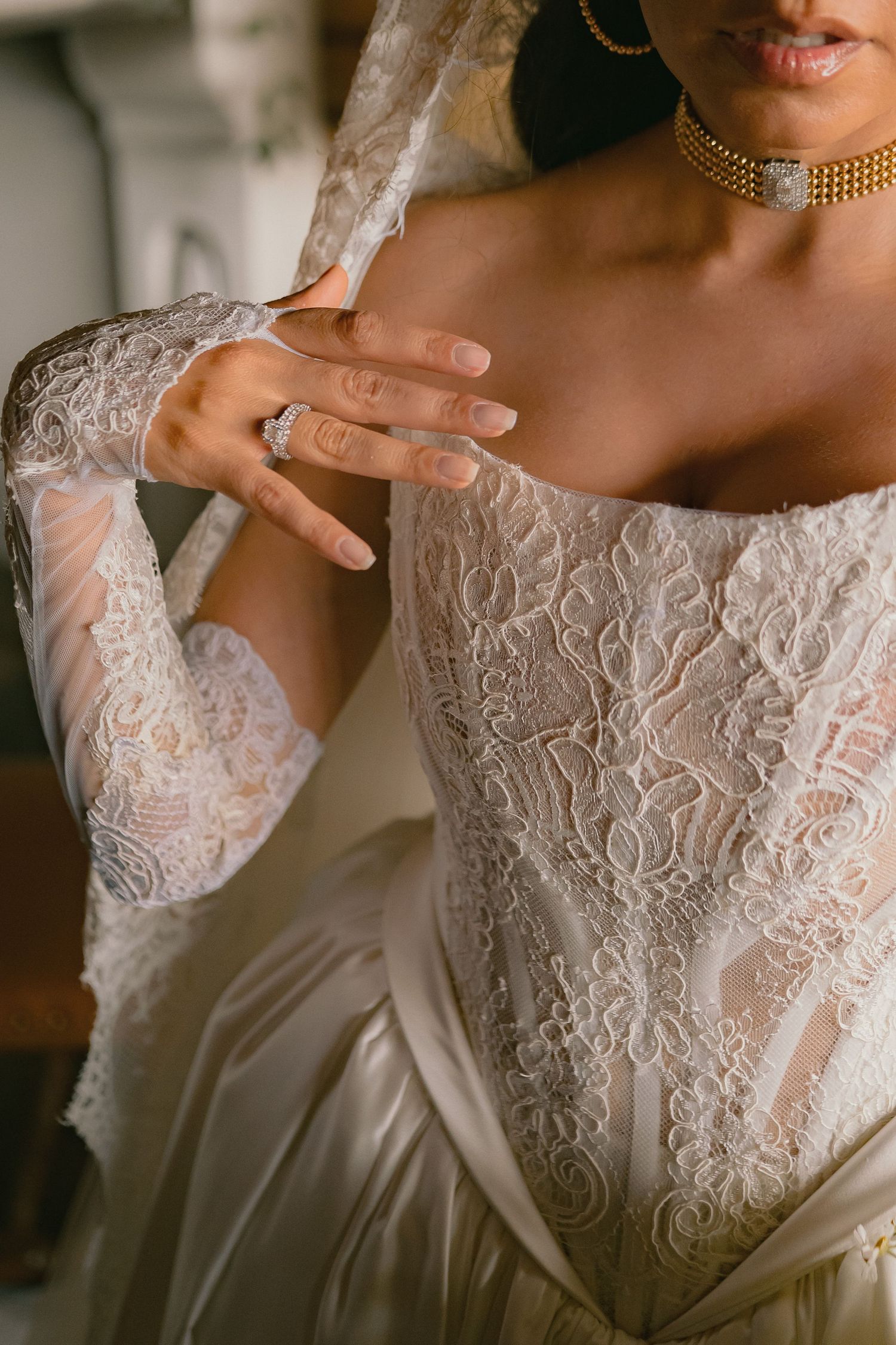 Close-up of bride in lace wedding gown with gold choker necklace and diamond engagement ring.